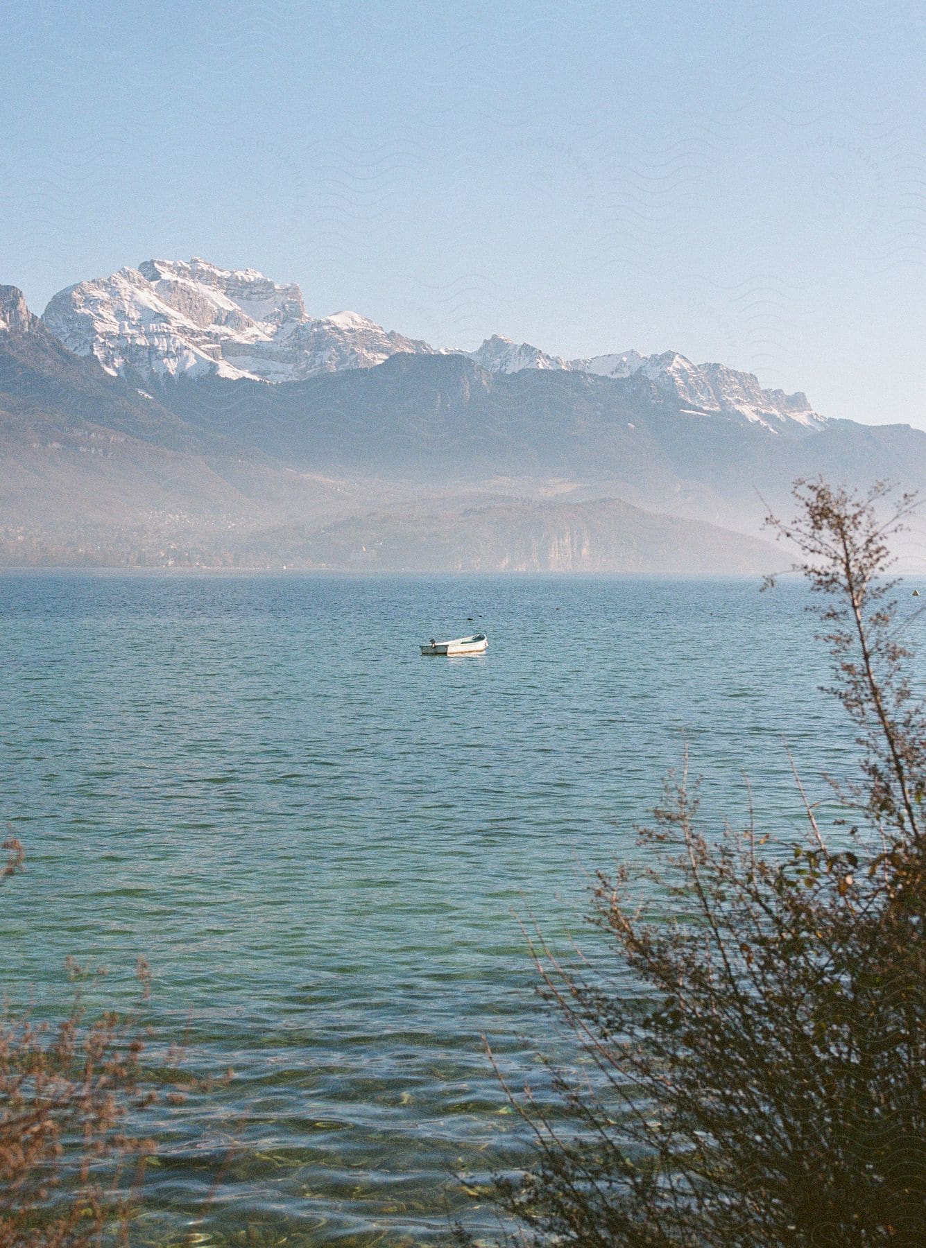 Scenery of a boat in the middle of the sea with a view of rocky mountains with snow on the horizon