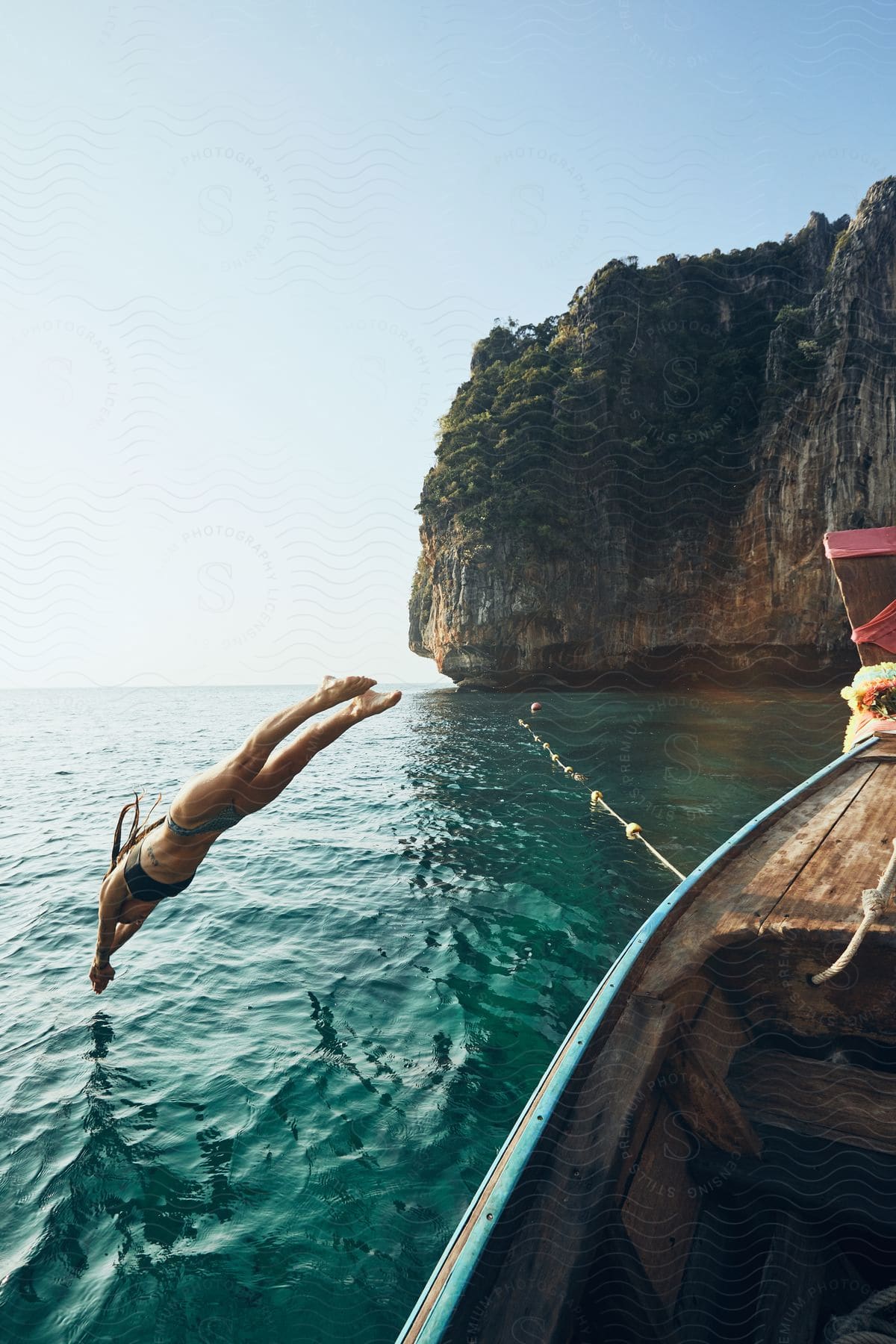 A woman in a bikini jumps into the sea from a boat in a bay.
