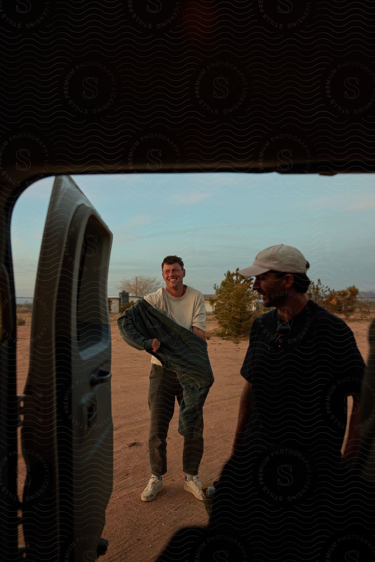 Two men near the open door of a van with the beach and ocean at their backs.