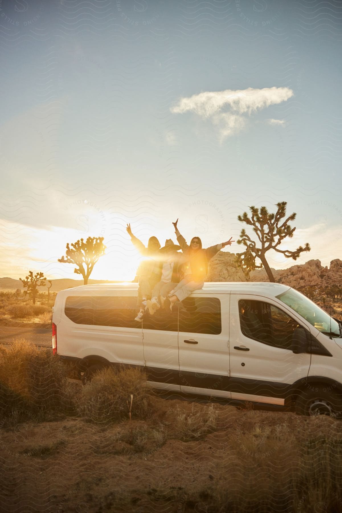 Three people sitting together on top of a van, posing for a photo, in the desert.