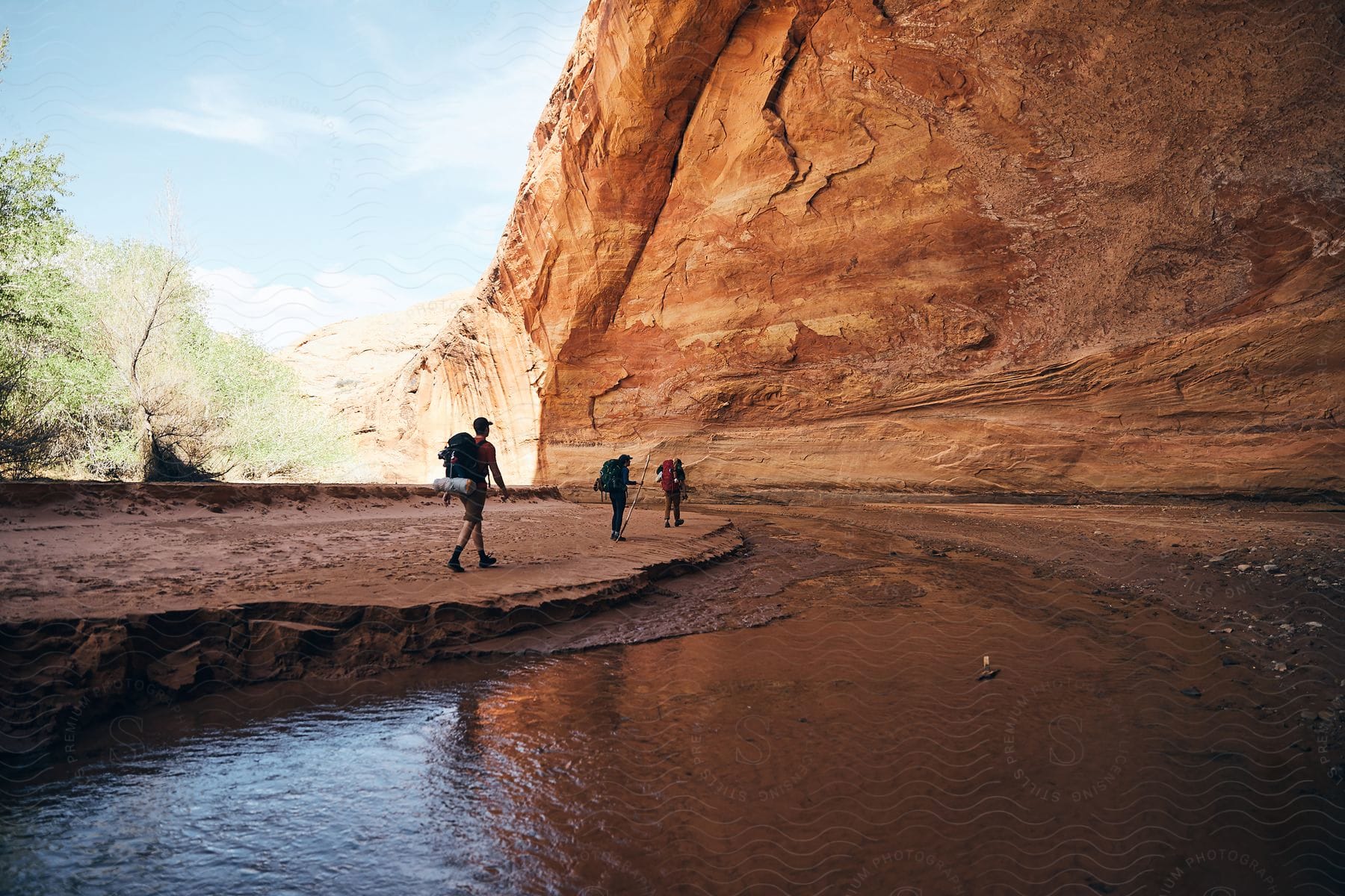 Three people walk beside a stream in a rocky gorge in the sunlight.