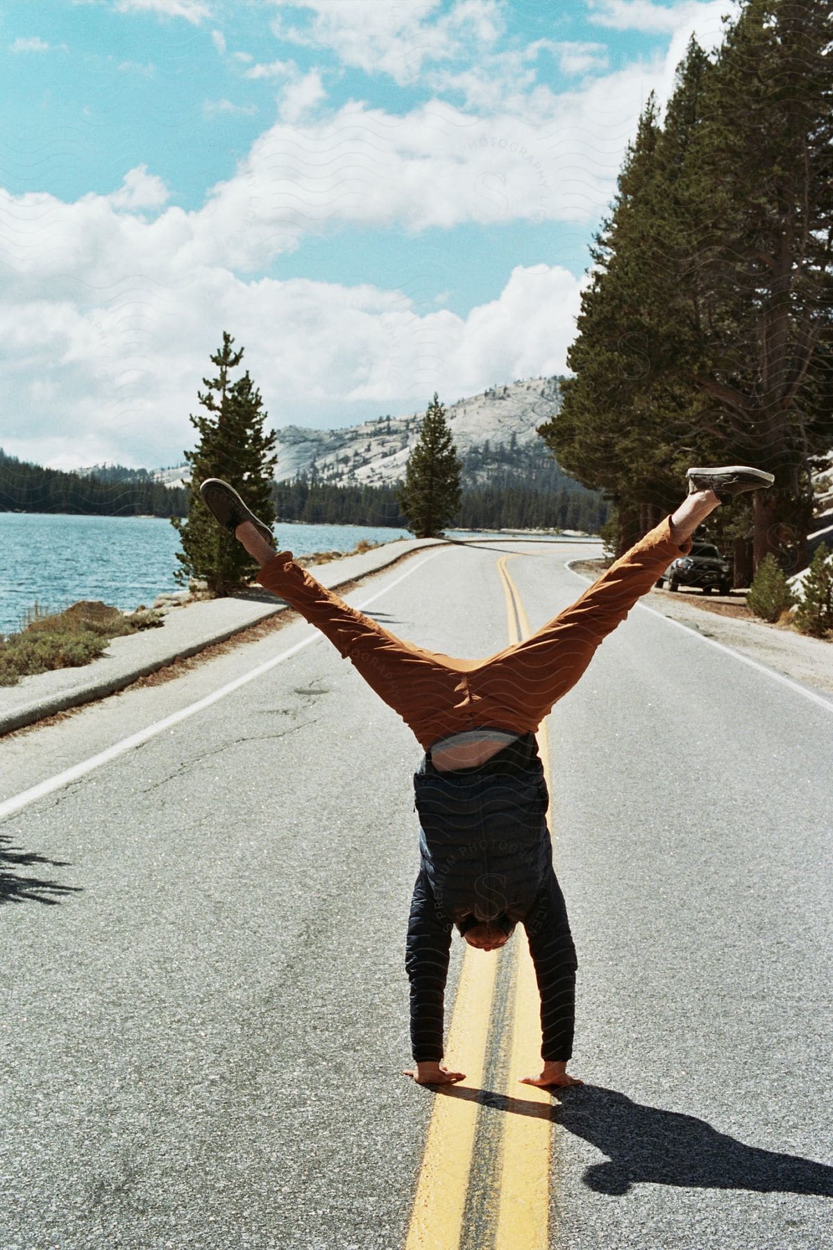 Man with both legs up in the middle of an asphalt near a lake and with mountains on the horizon