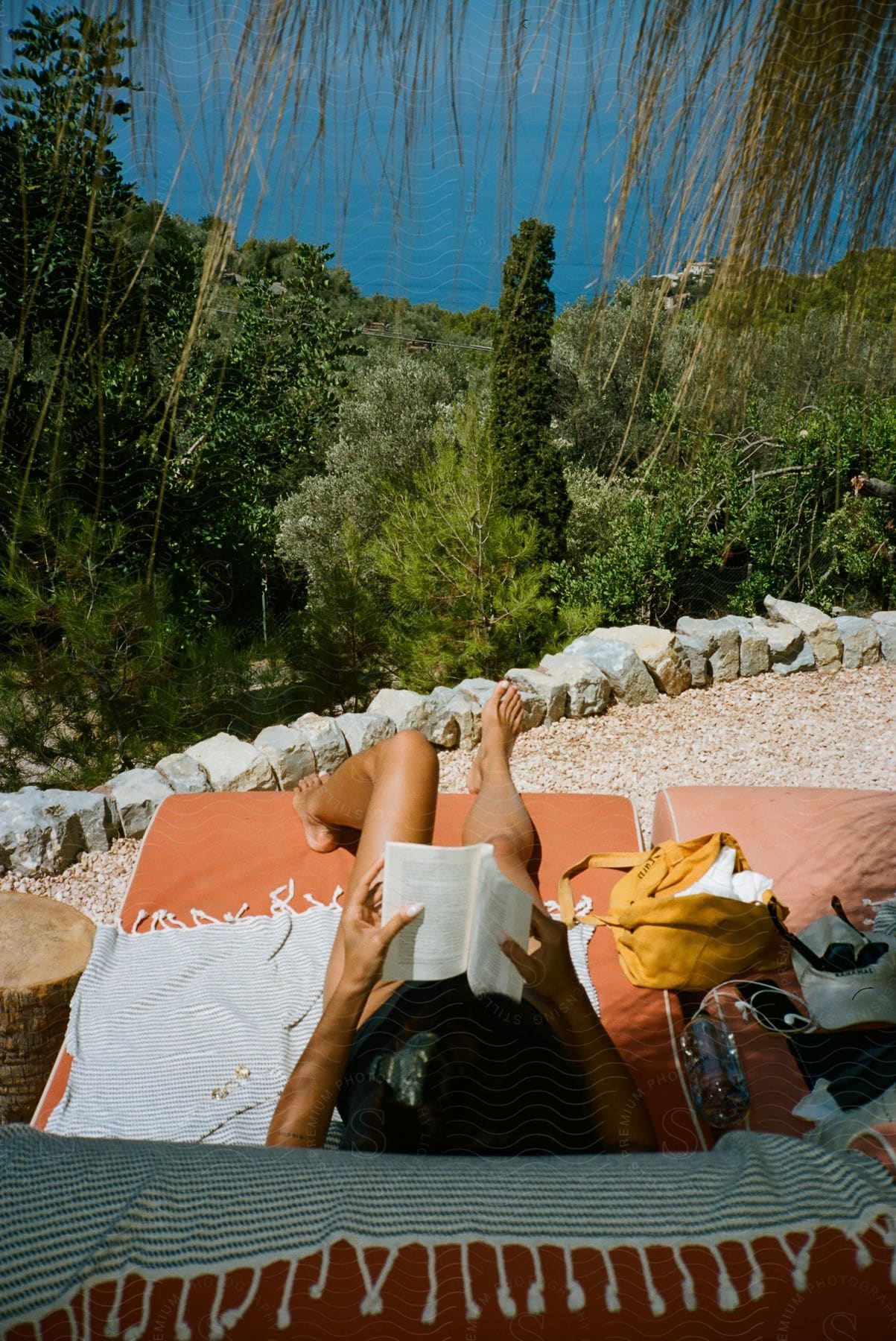 A woman in a bikini sunbathes while reading on a hill overlooking the bay.