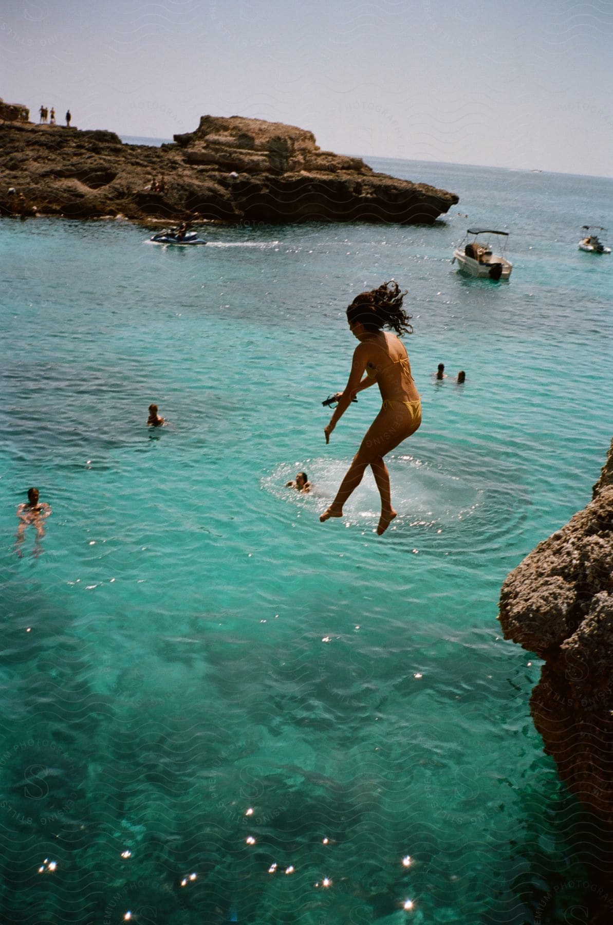 A woman in a bikini jumps off a cliff into the water."