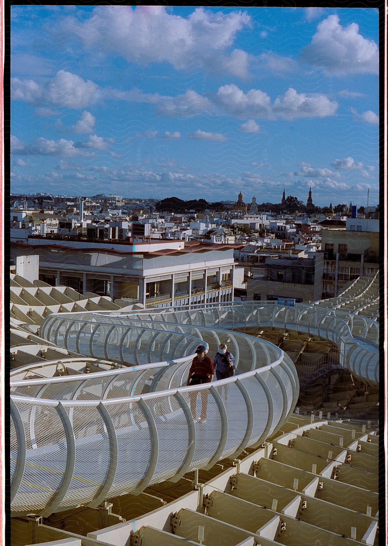 Panorama of a Setas bridge in Seville with two people walking and overlooking a city.