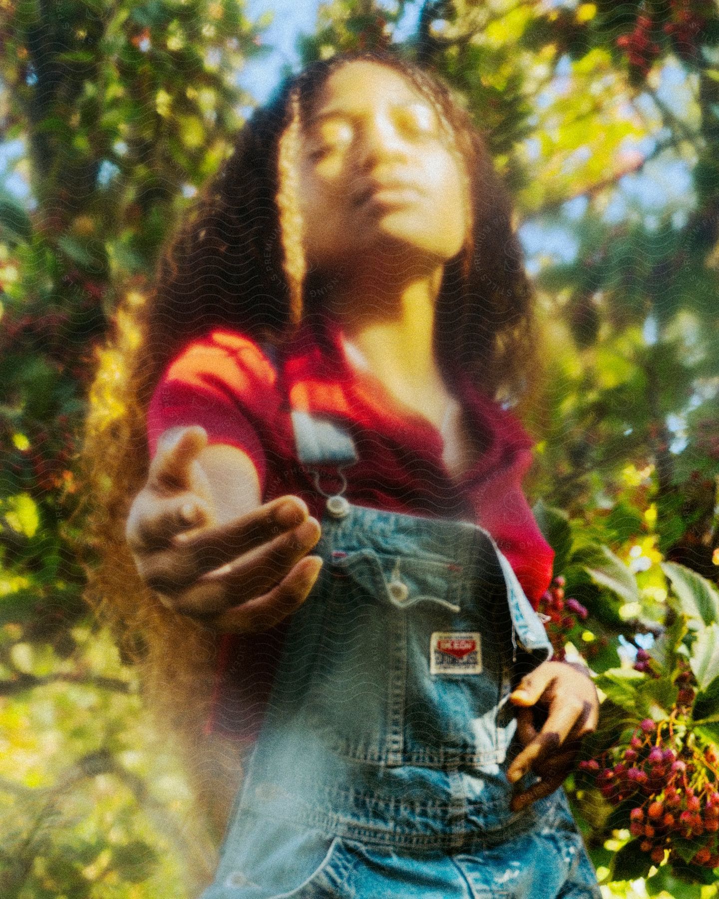 A person with closed eyes reaches towards the camera in a dreamy, sunlit garden setting.