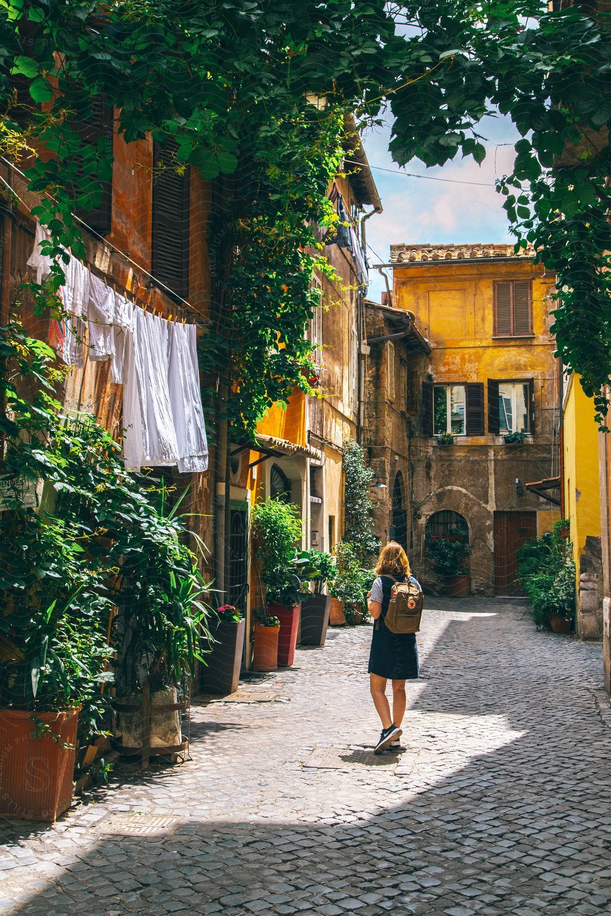 A woman with a backpack in an alley of some houses with many plants in pots