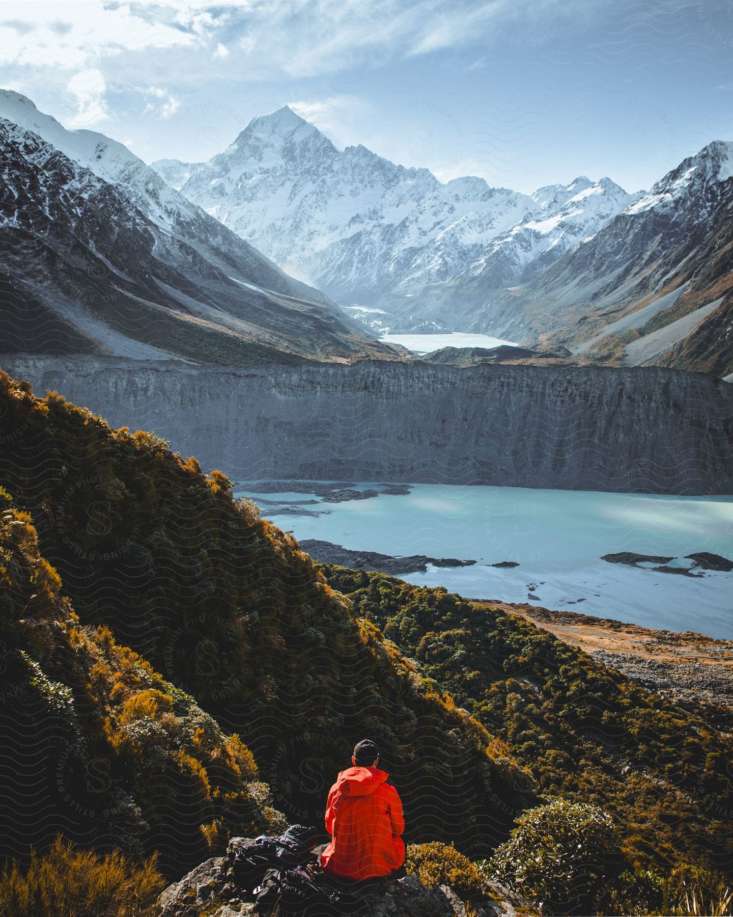 Hiker sits on a mountain overlooking a frozen lake with mountains in the distance