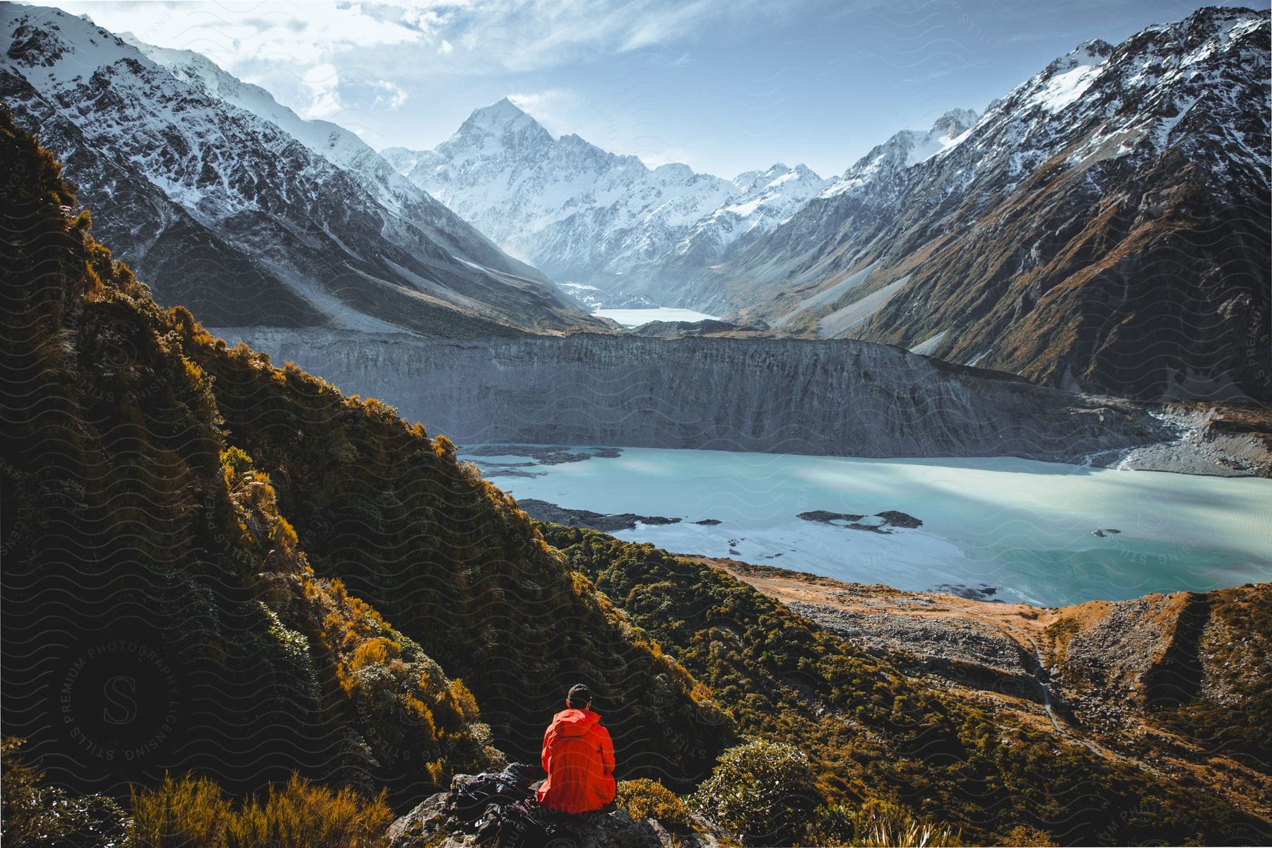 Stock photo of man wearing a red jacket sits on a rock watching hooker valley within mount cook national park