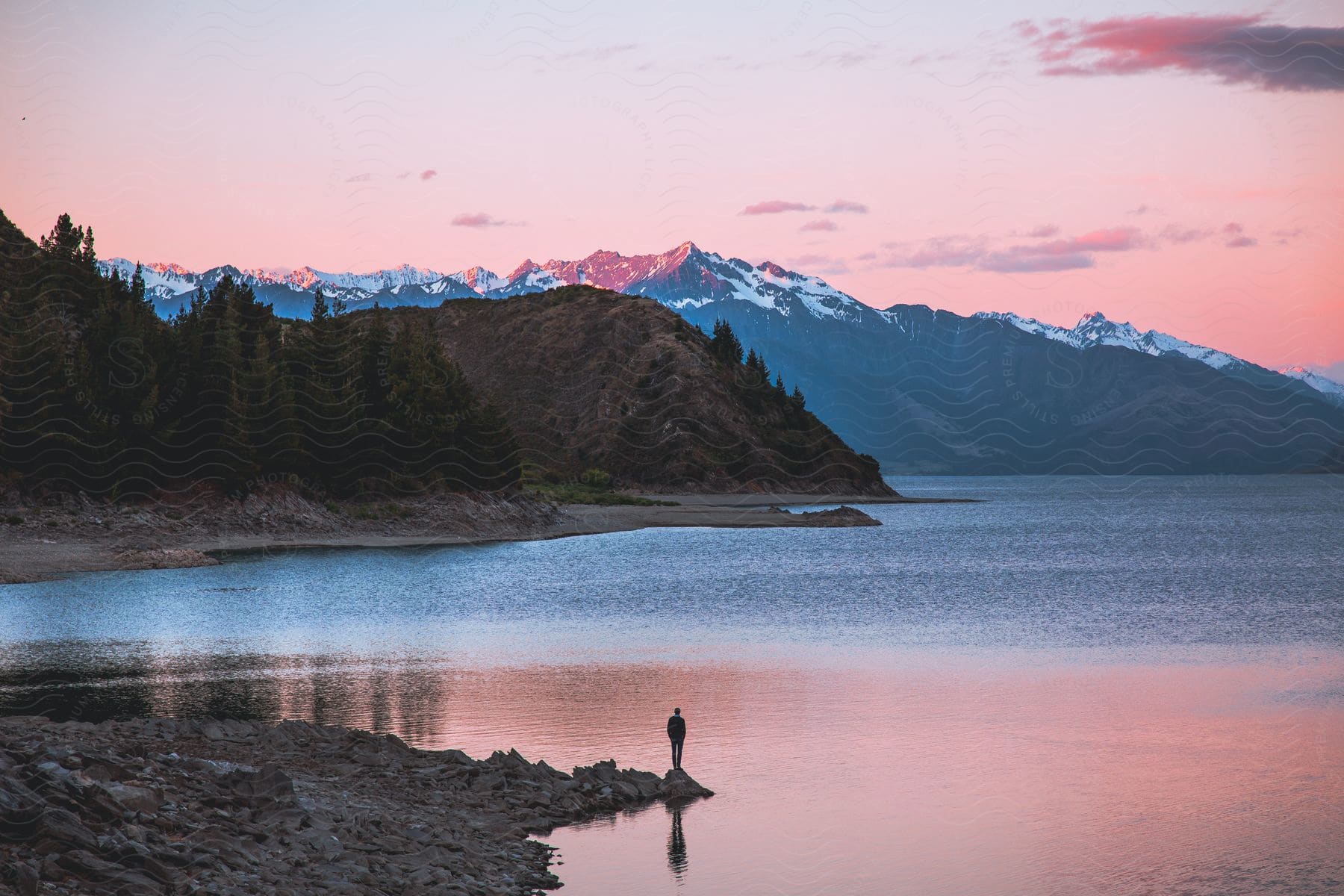 Landscape of a person on a rock by the lake with mountains around on a red sky day.