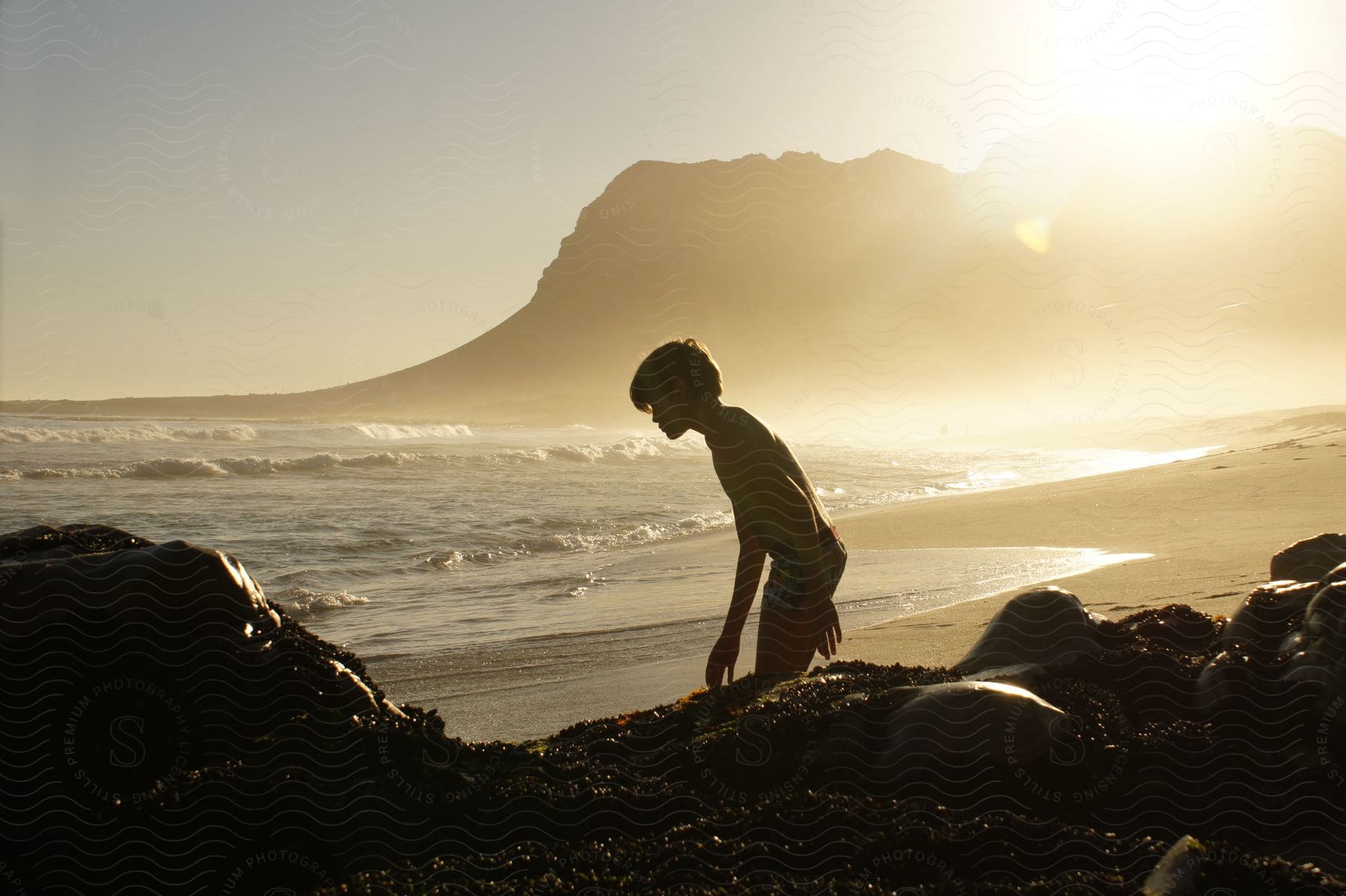 Silhouette of a boy on the beach as the sun shines over the promontory in the distance