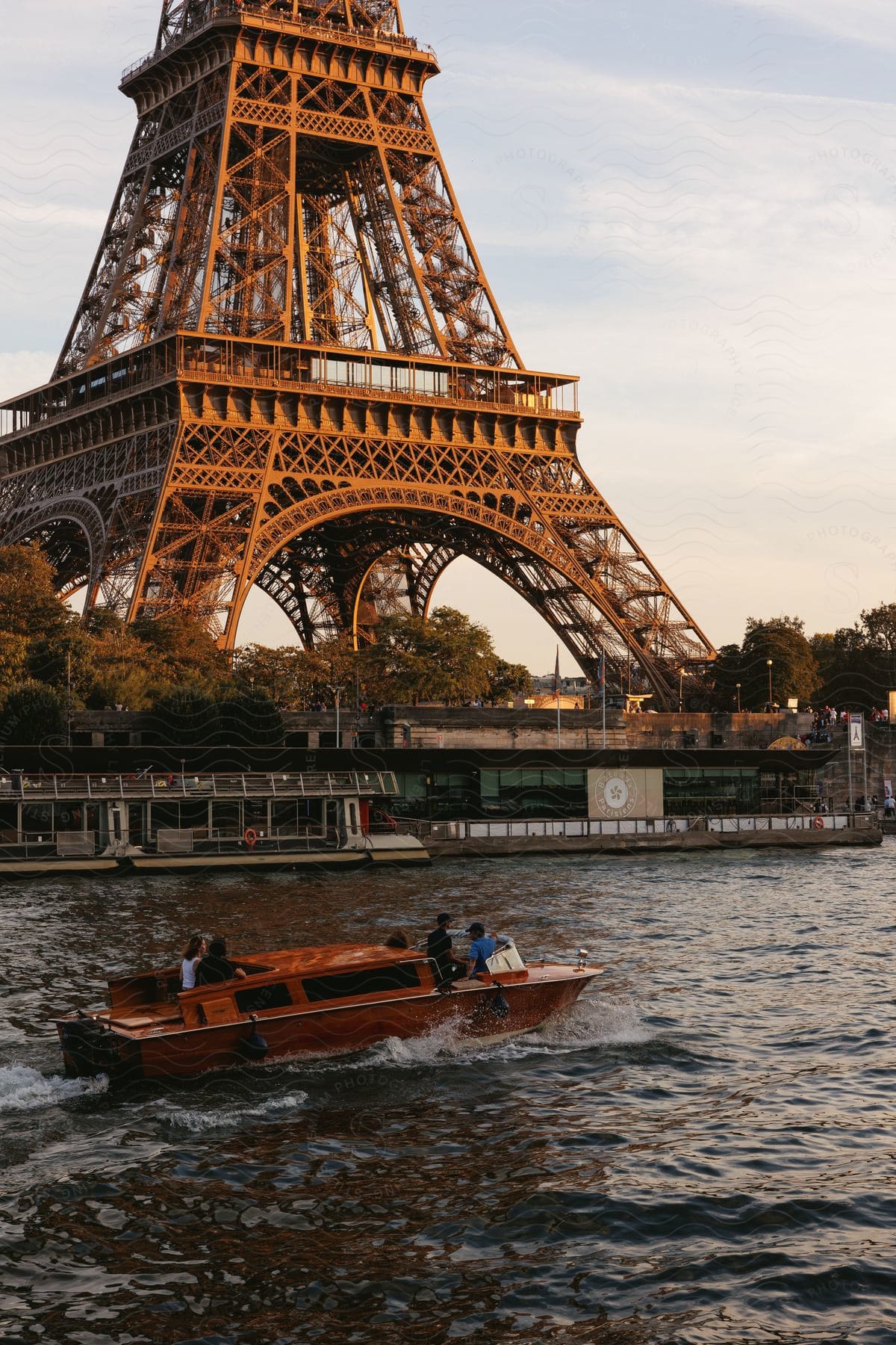 A boat with people sails down the river in front of the Eiffel Tower at sunset.