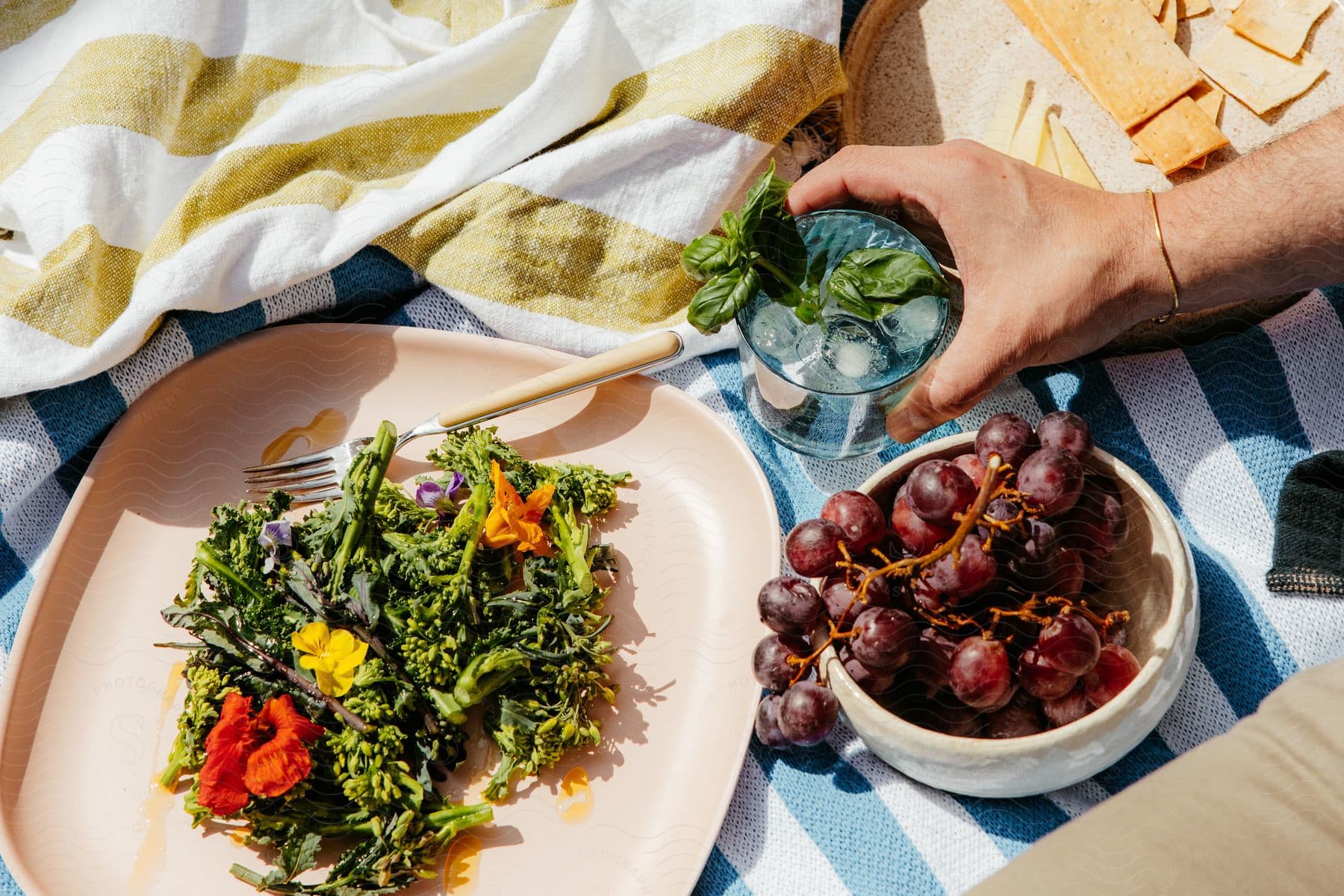 A man holds a drink next to a bowl of grapes and salad on a plate