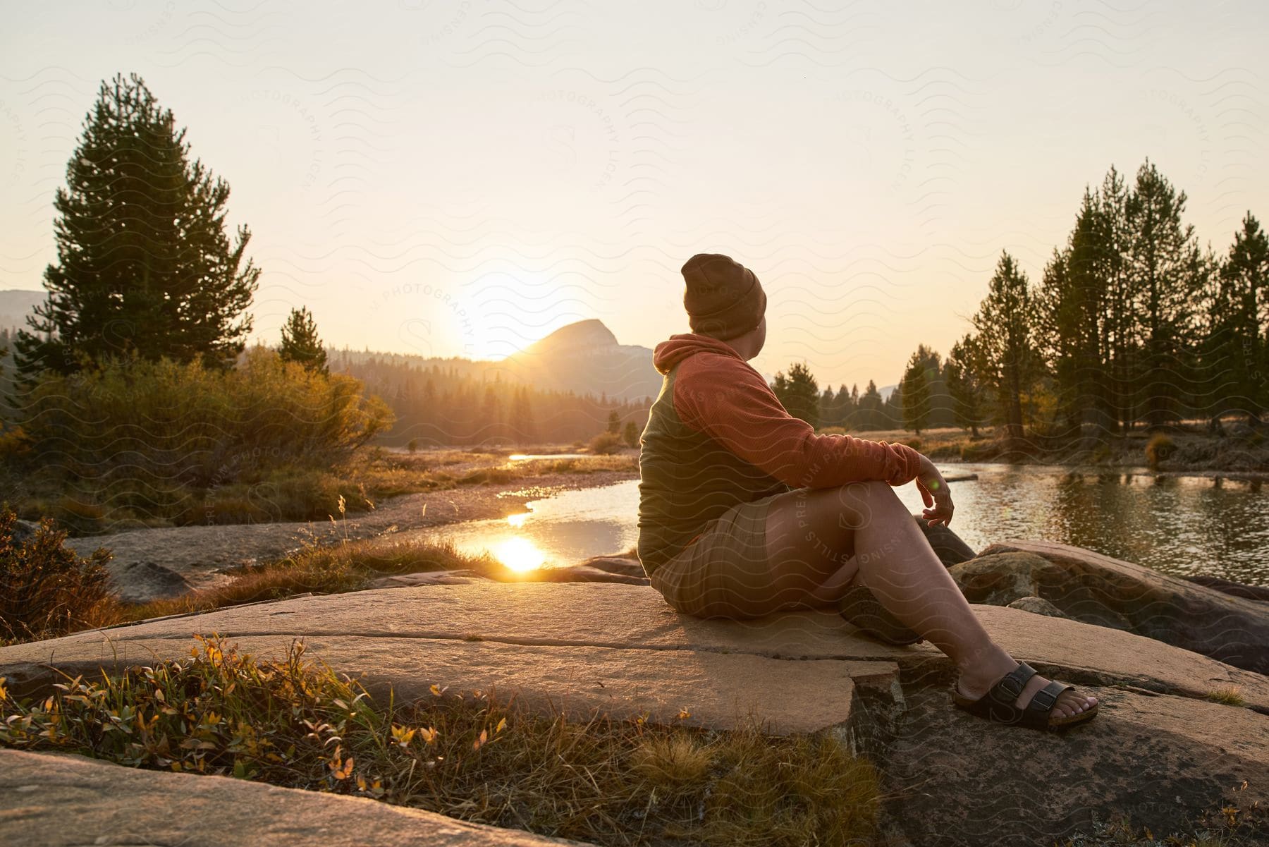 A man sitting on a rock looking at the sunset going down near the mountains