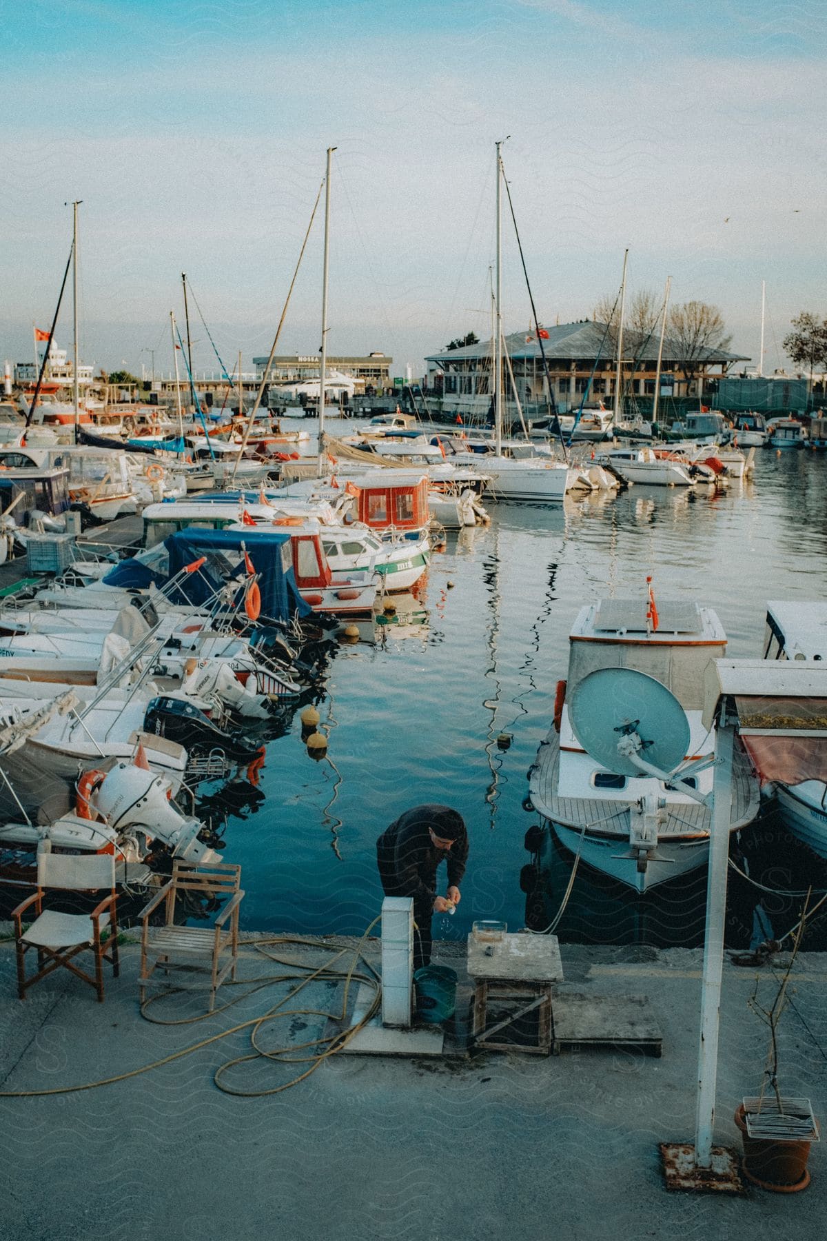 A man on the dock with many boats in the marina and a building along the coast