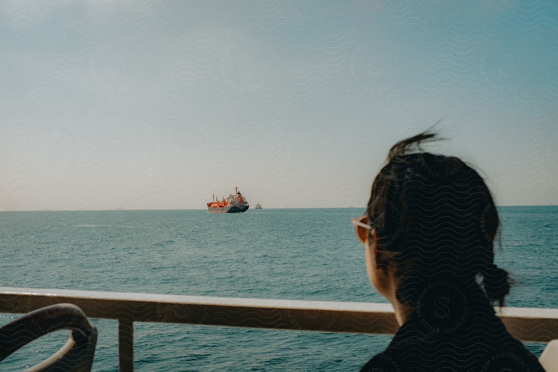 A woman on a boat, looking at a freight boat in the distance.