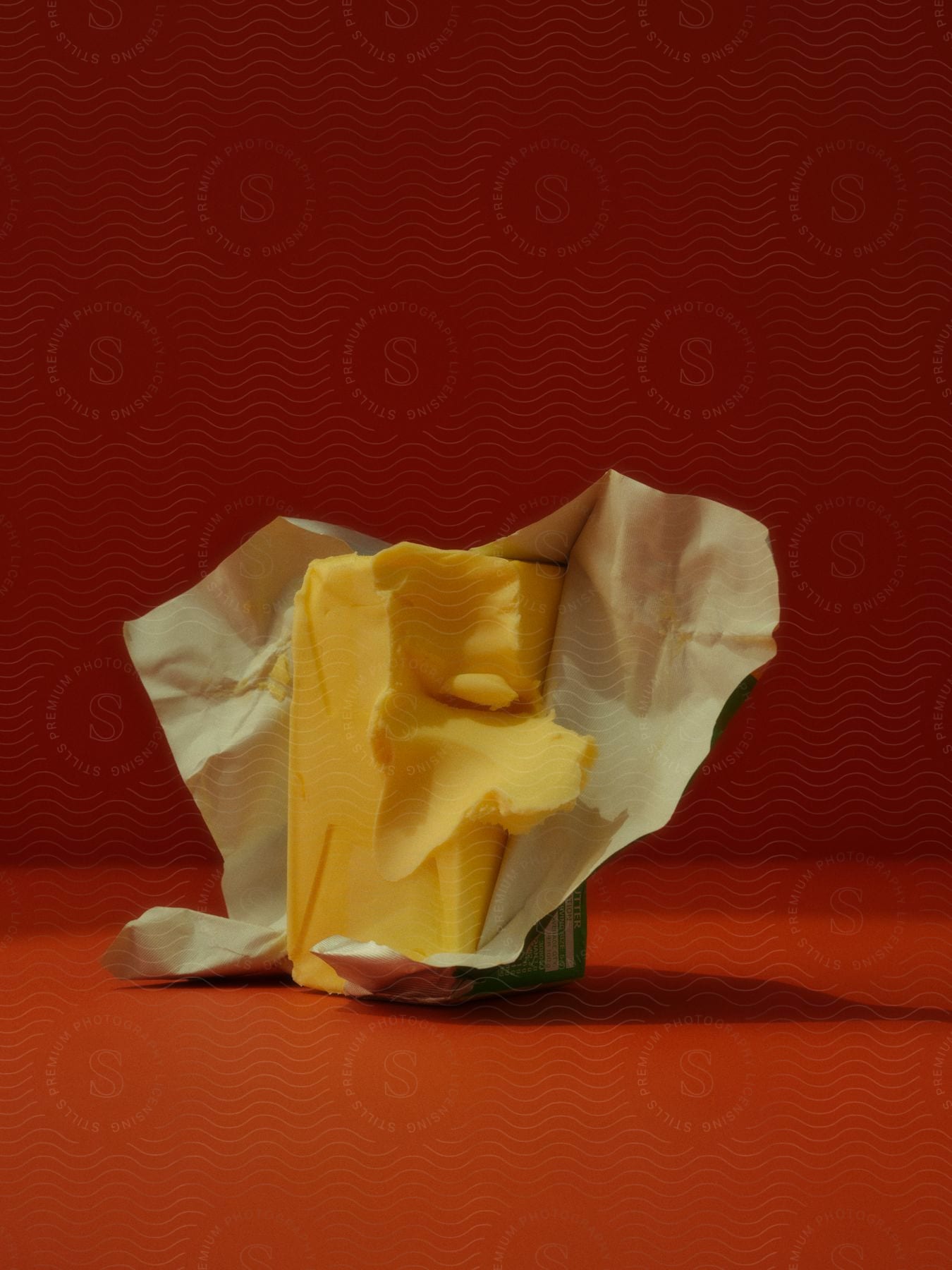 A golden block of butter sits on a red table with a faint checkered pattern