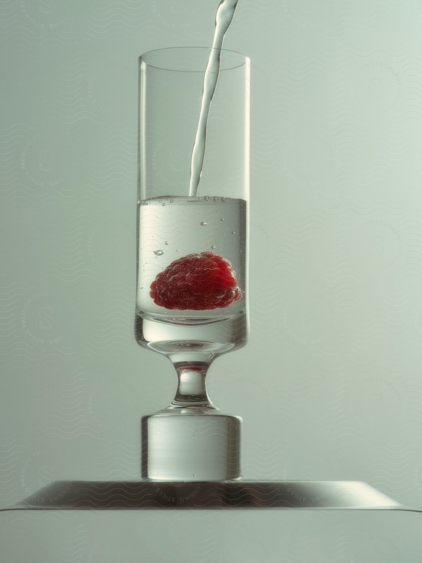 Liquid flowing into a glass with a raspberry in it.