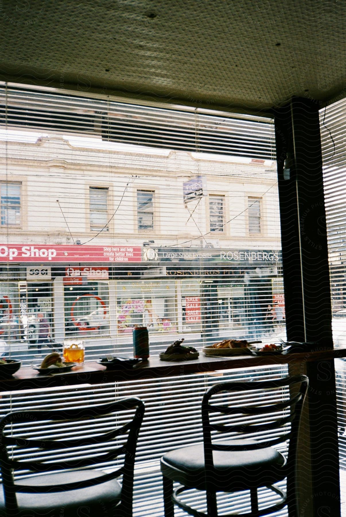 a storefront with a table and chairs visible through a large window with blinds