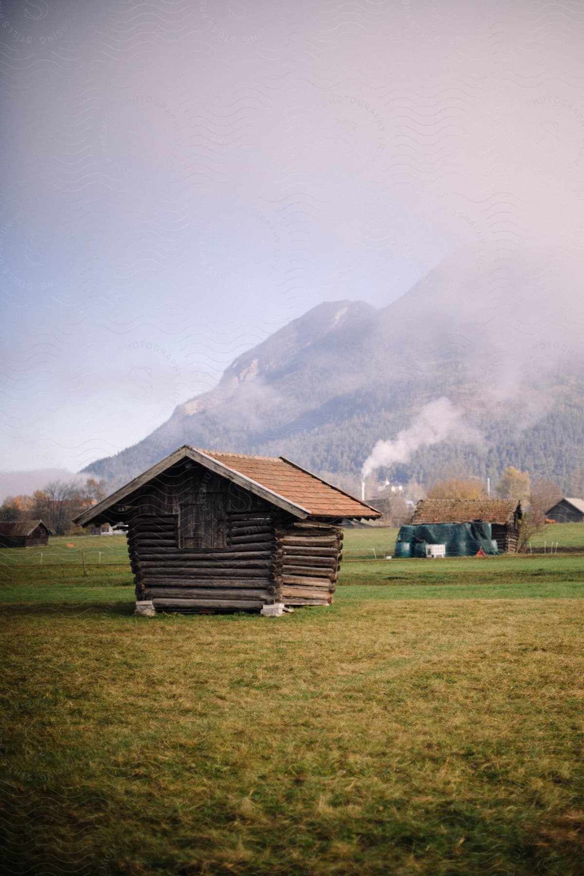 A log farm building at the base of a forested mountain.