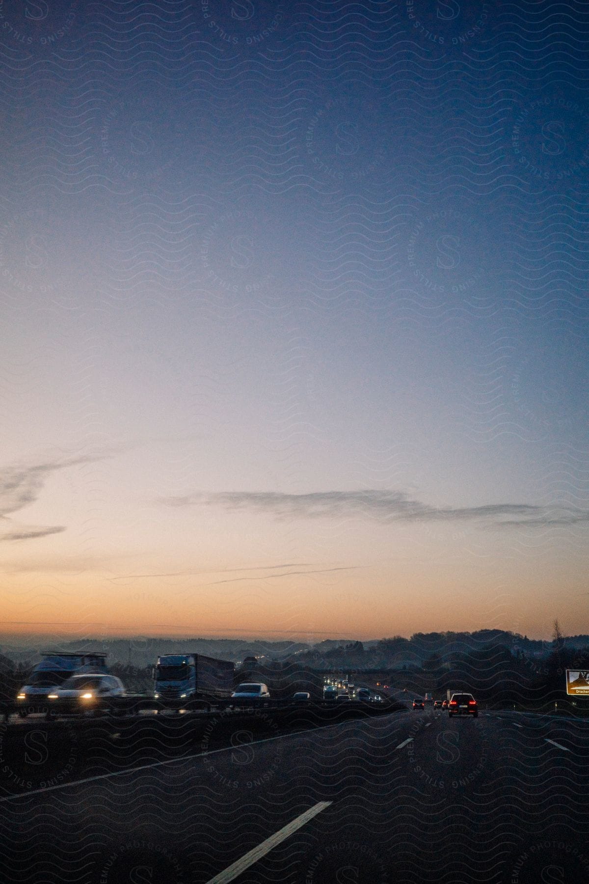 s a highway filled with cars and trucks traveling during dusk, with the sky ablaze in orange, pink, and purple hues.