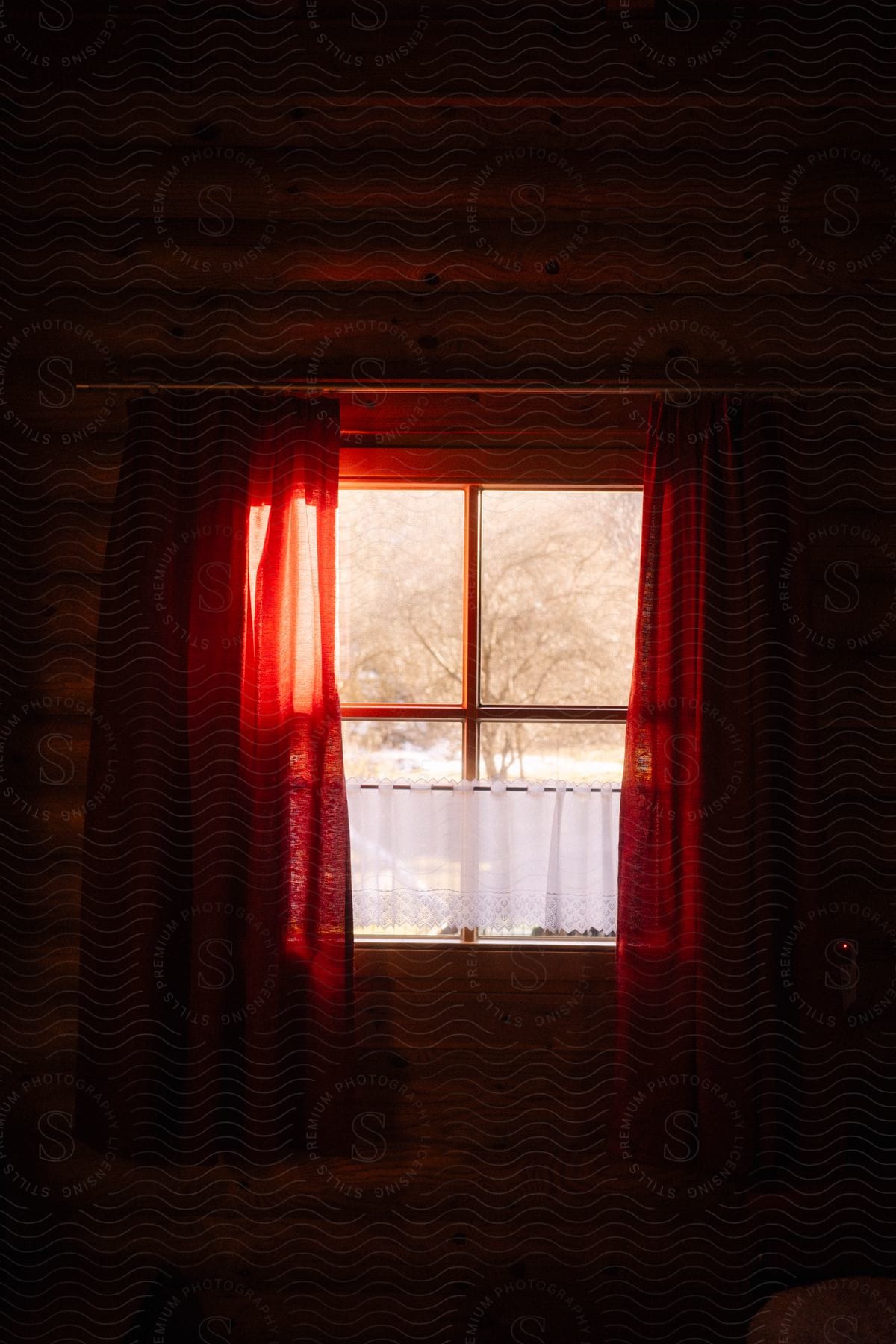 The sun shines through a window with red curtains on a cabin style wall