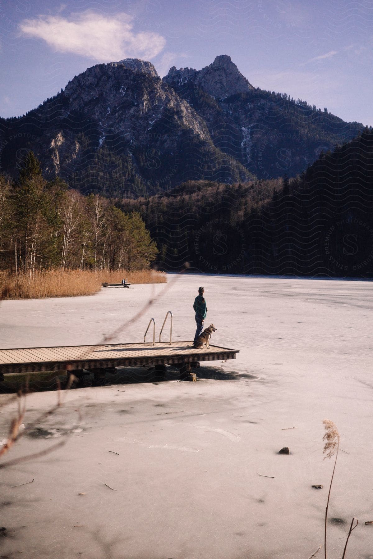 Man next to his dog on a dock on a frozen lake with mountains around