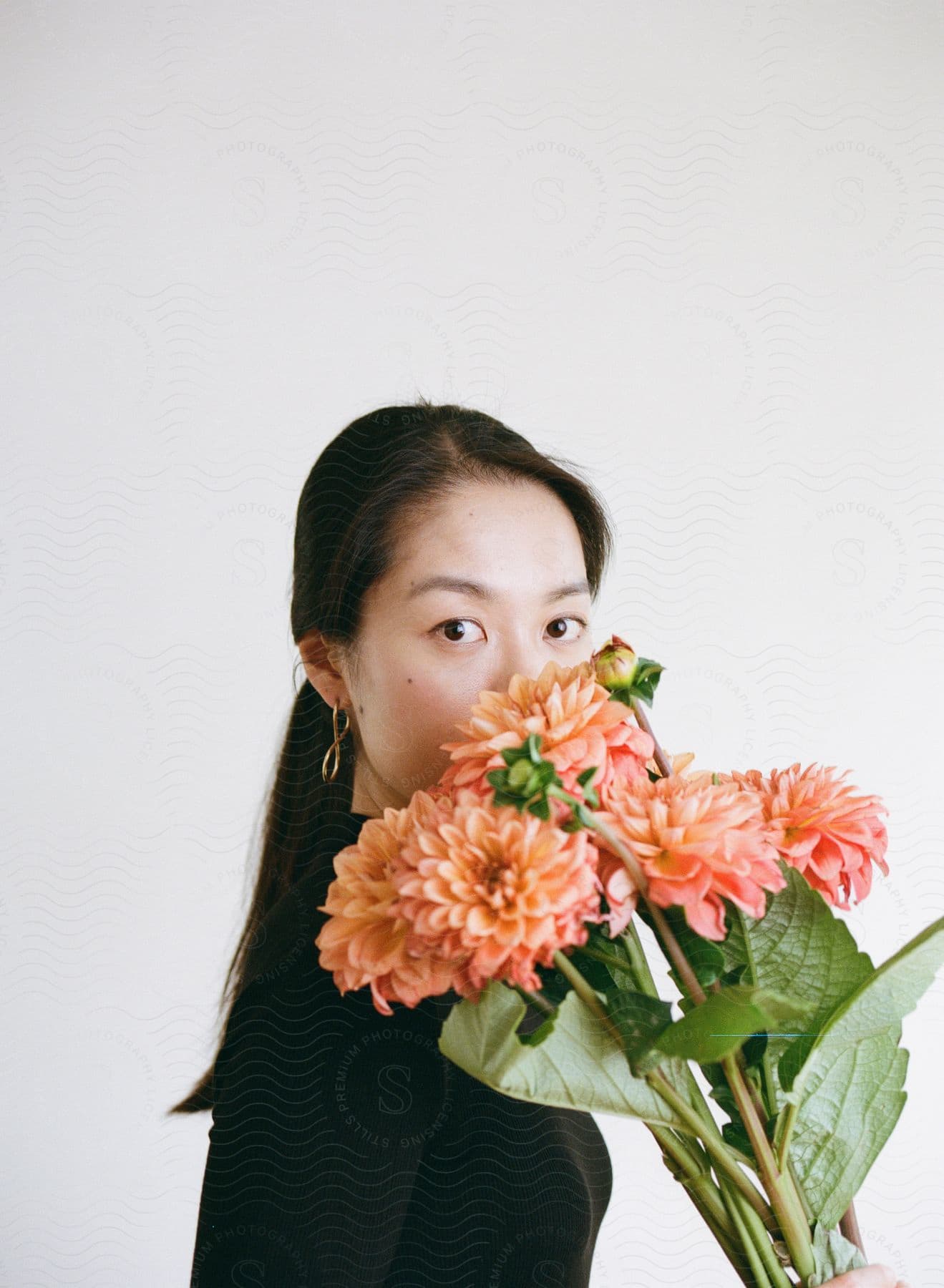 A woman is looking forward while smelling a bouquet of orange-colored flowers on a white background
