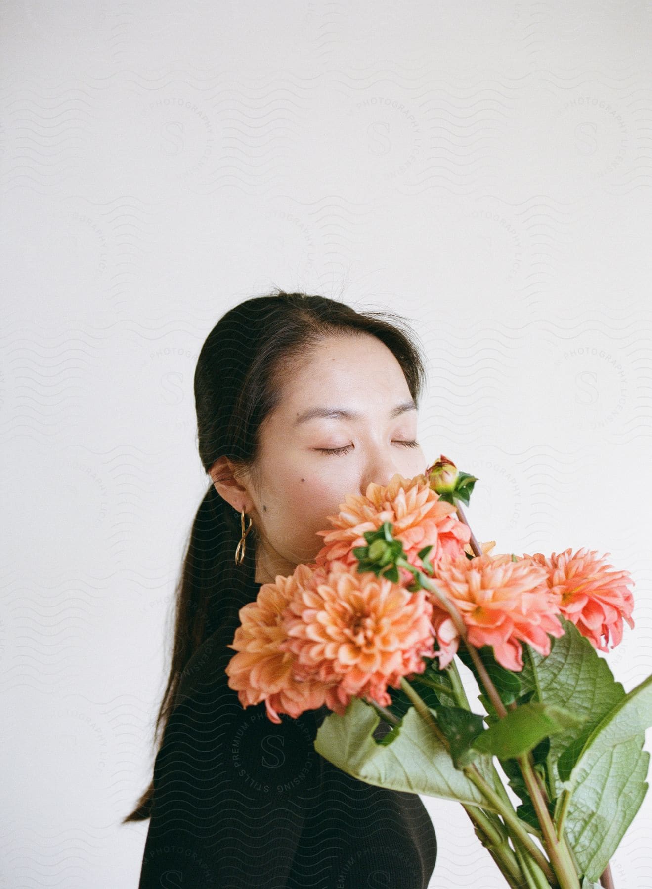 A woman has her eyes closed and is smelling a bouquet of orange flowers