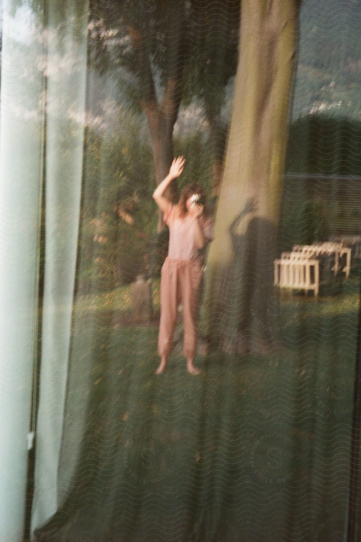 Window reflection of a young woman taking a selfie outside in a yard.