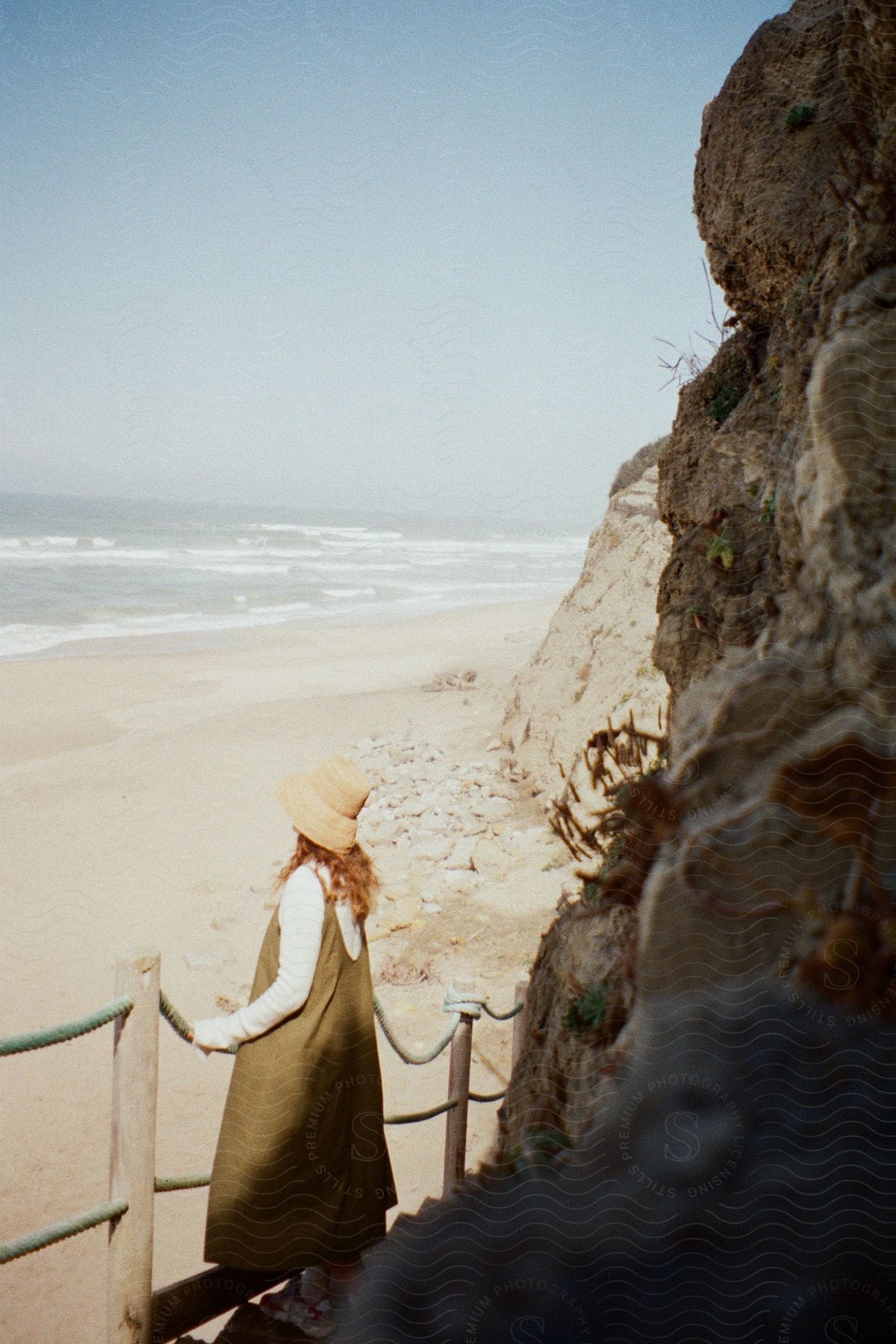 A woman in a long dress and a sun hat looking at a beach.