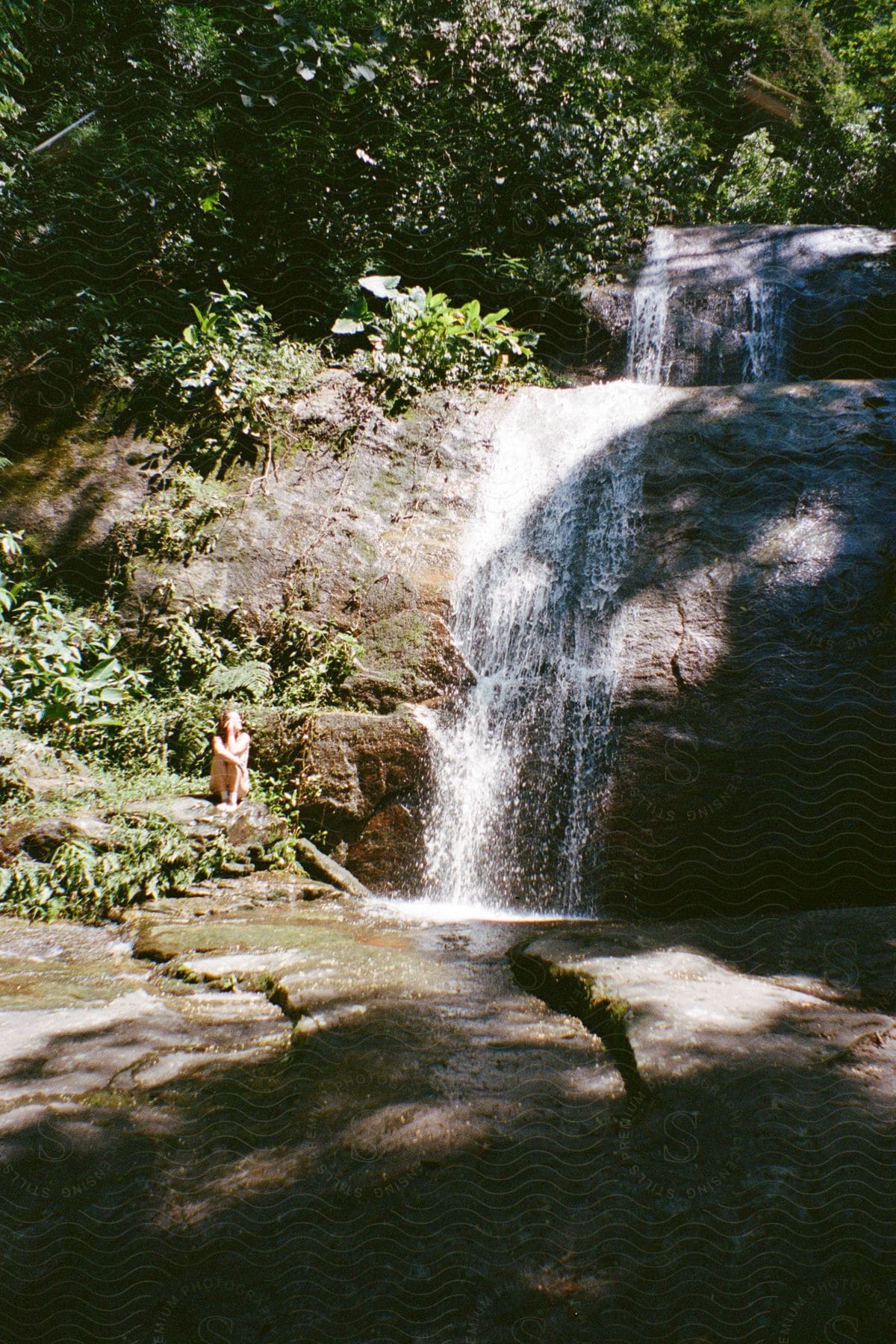 Woman sitting next to a stream as a waterfall flows over a cliff