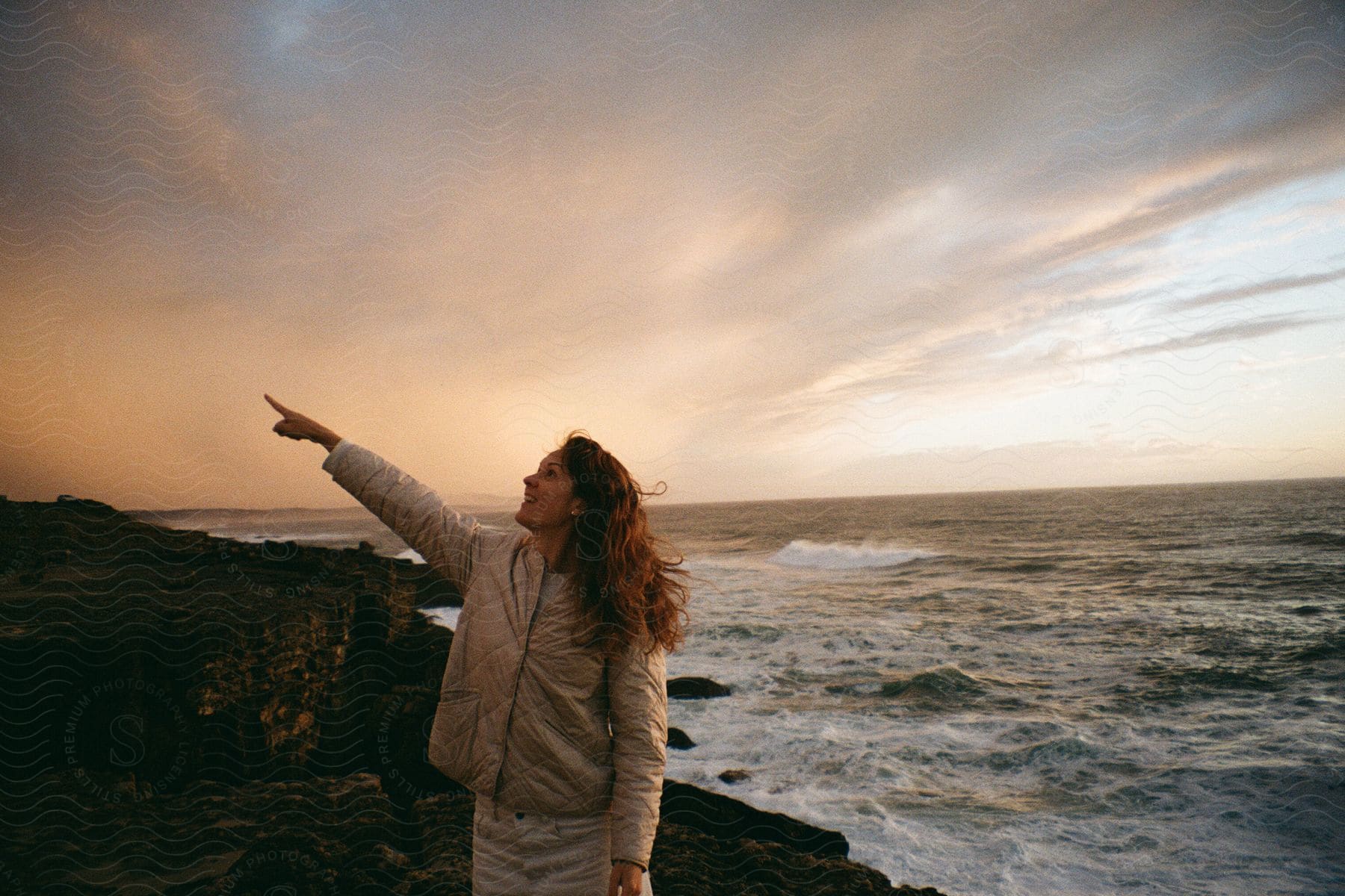 Woman pointing up while standing on the seaside coast in a yellowish morning sky