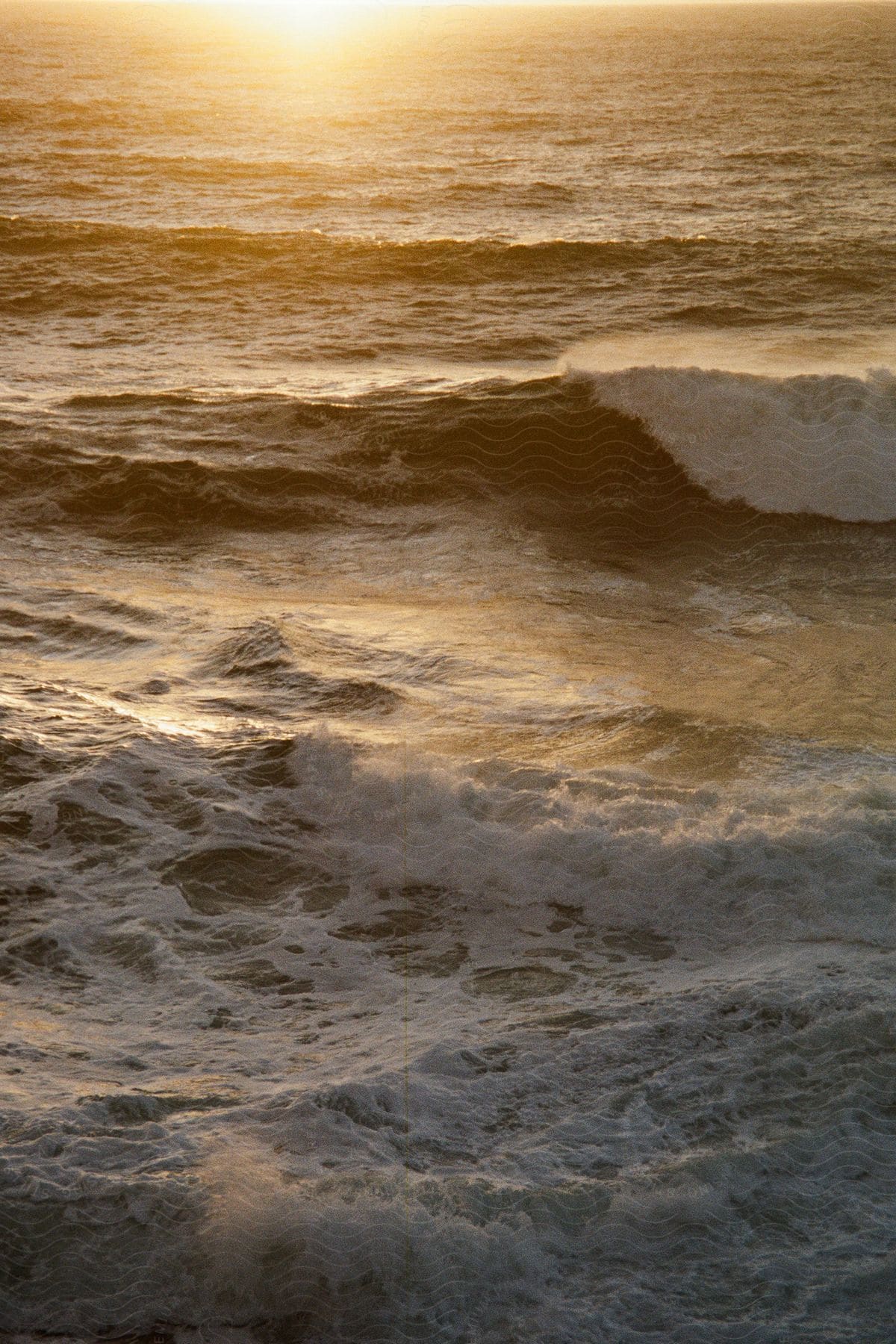 Ocean landscape with foamy waves and sunset reflecting on the horizon