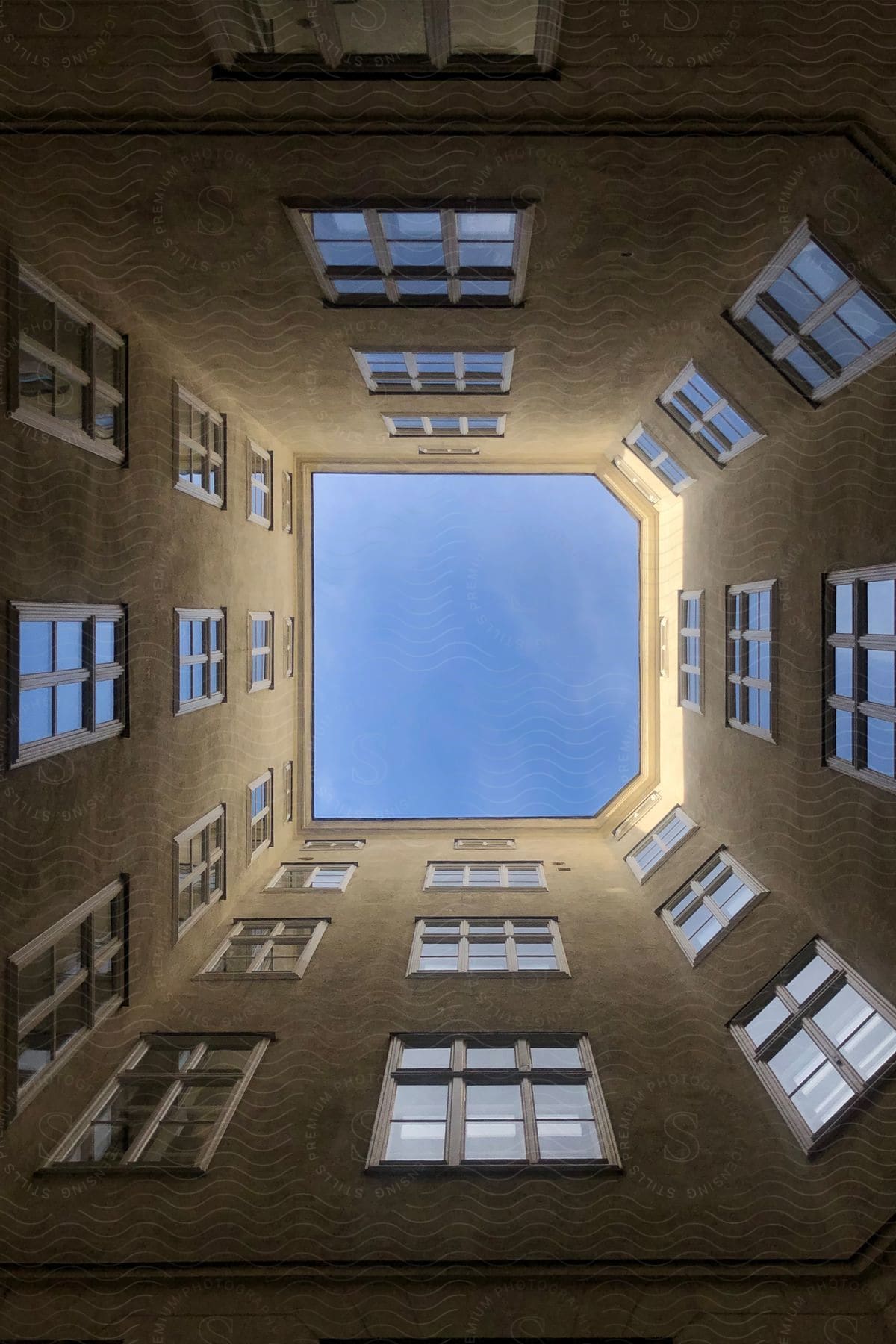 Upward view of the exterior architecture of a building with windows and blue sky.