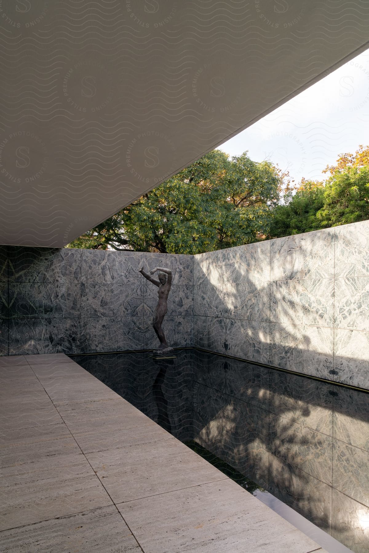 Sculpture with arms raised overhead outdoors in the corner of reflecting pool