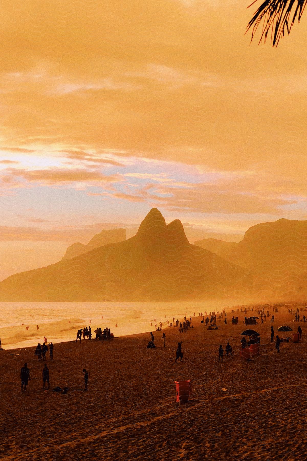 Sunset at a beach with silhouettes of people and mountains in the background.