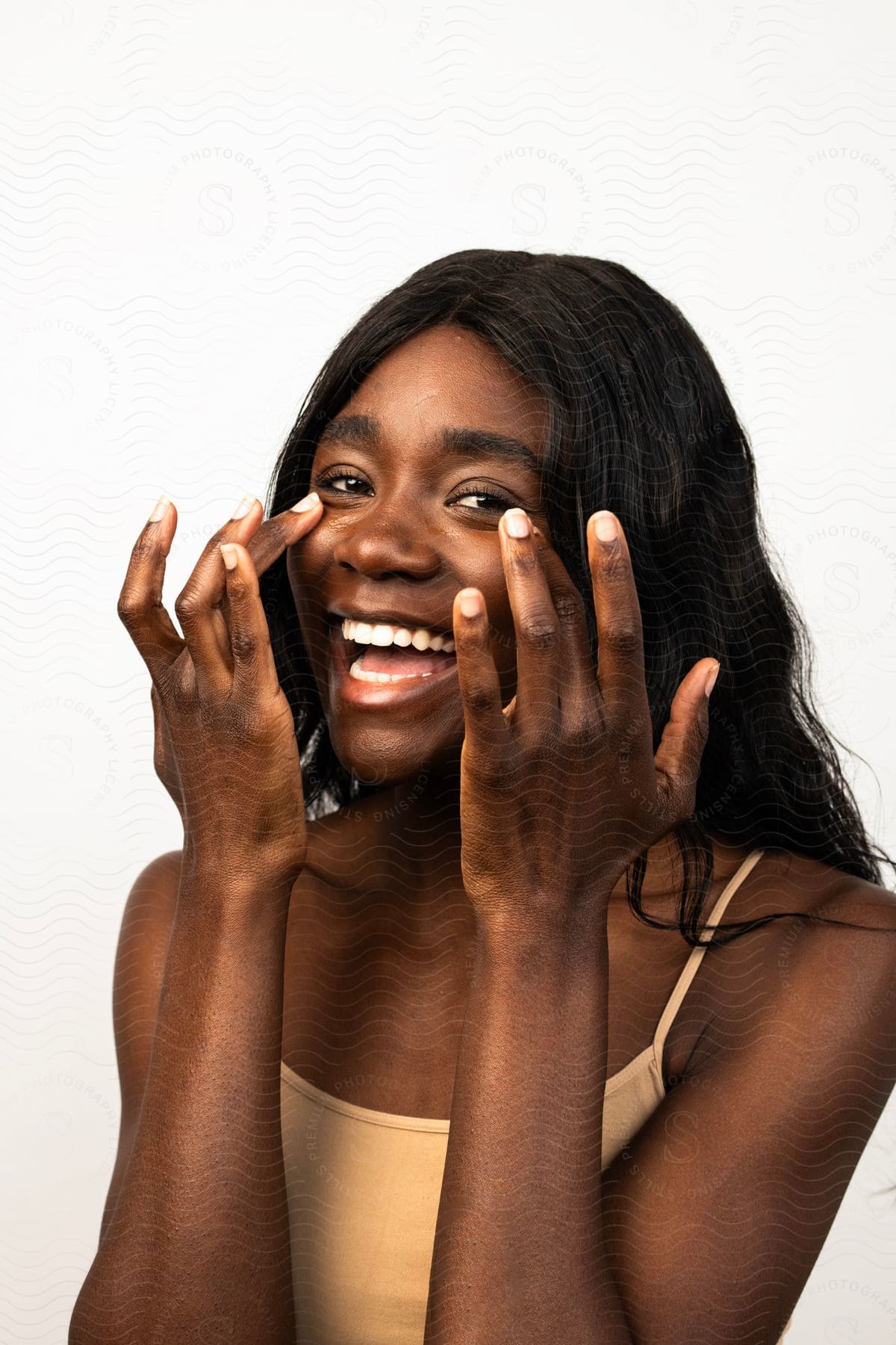 Happy woman applying cream to her face with both hands, against a light background.