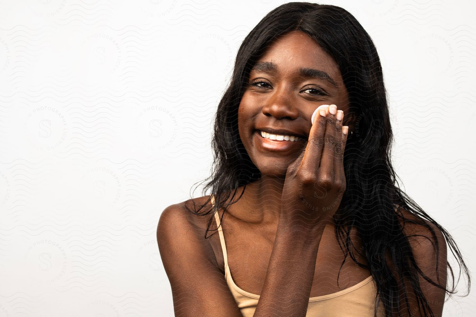 Woman smiles as she rubs skin cream on her cheek with her fingers