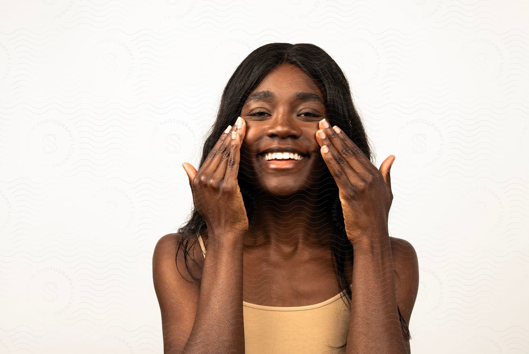 Woman applying facial cream, with a wide smile, against a light background.