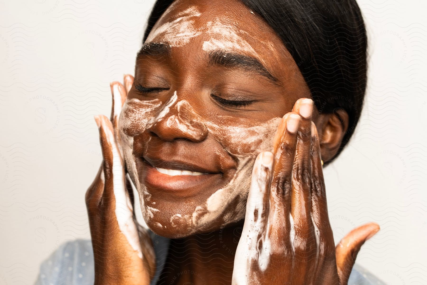 A portrait of a woman smiling while washing her face.
