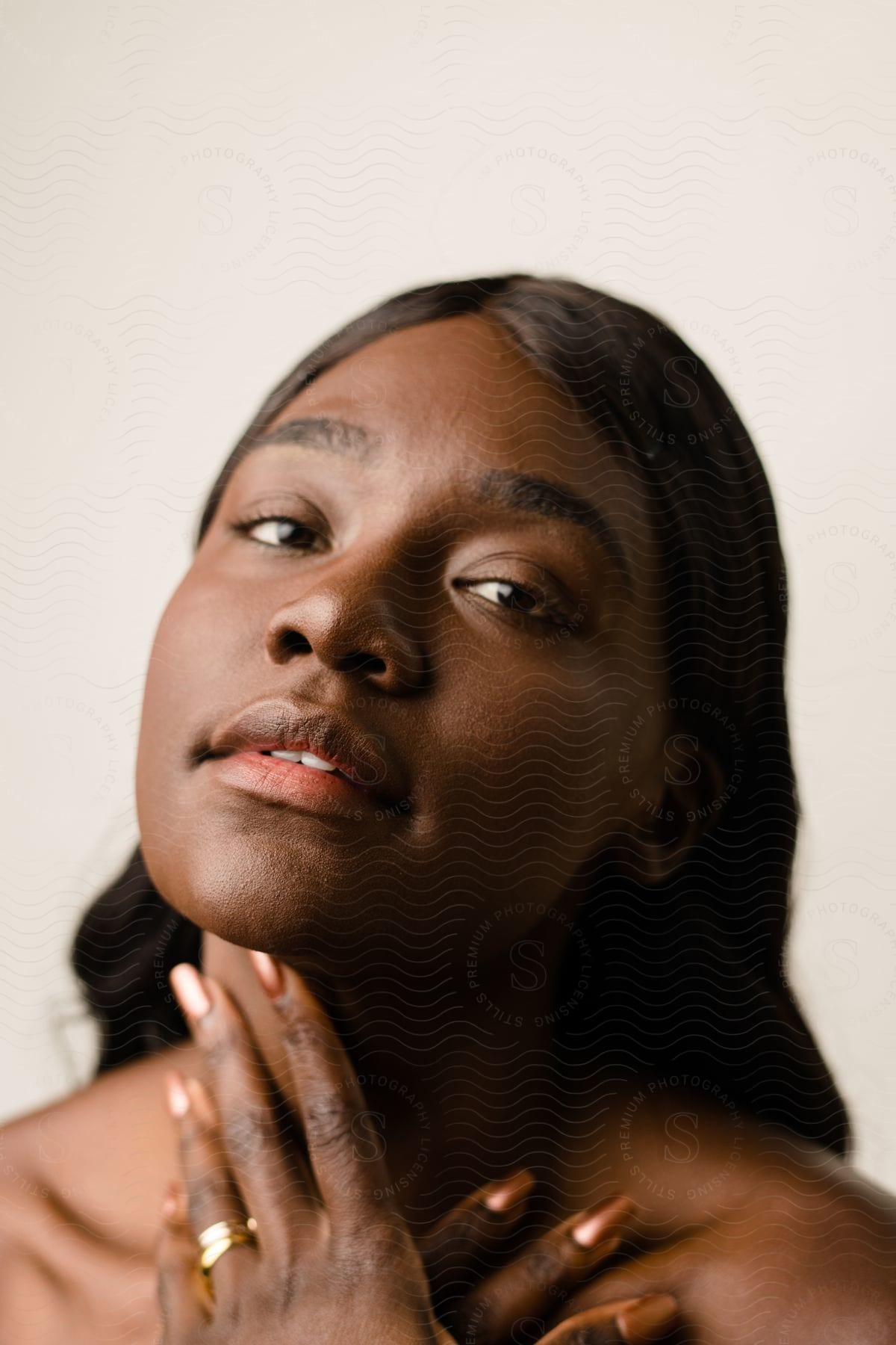 Close-up portrait of a woman with her hand on her neck against a light background.