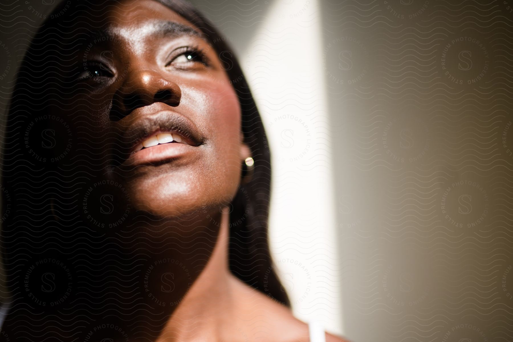 Close-up of a woman looking upwards, with sunlight casting a shadow over her face.