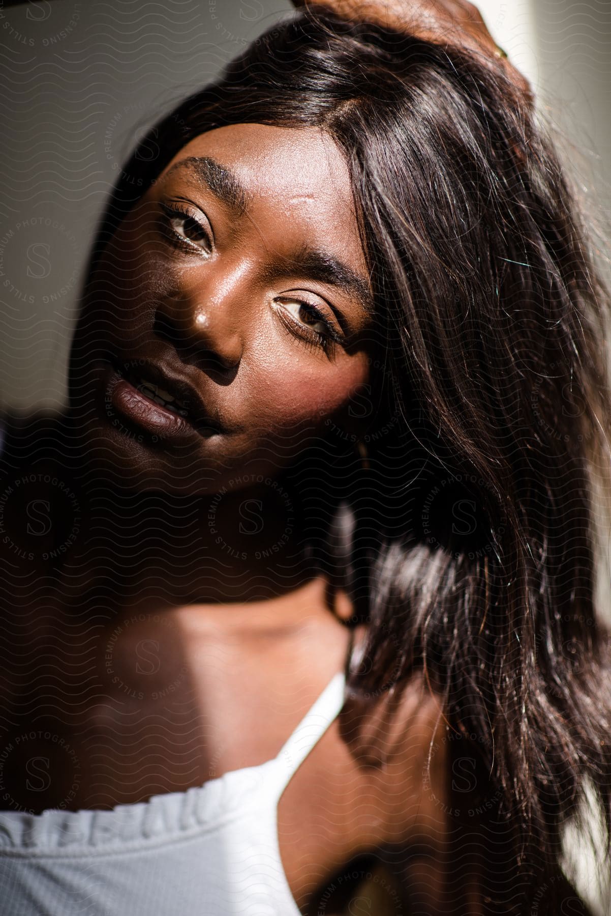 Portrait of a woman with one hand in her long, dark hair that is illuminated by a sunlight source.