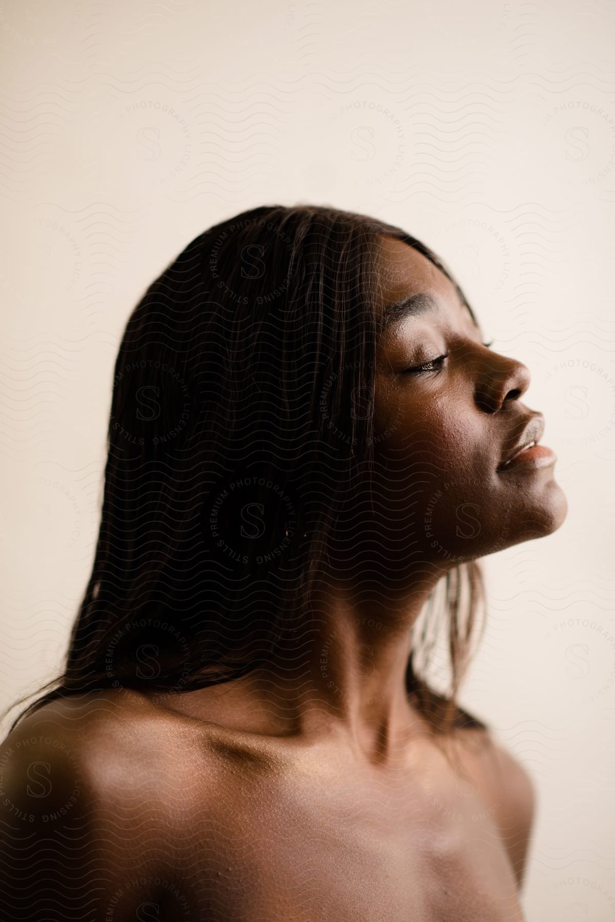 Side portrait of a shirtless young black-haired woman on a white blurred background