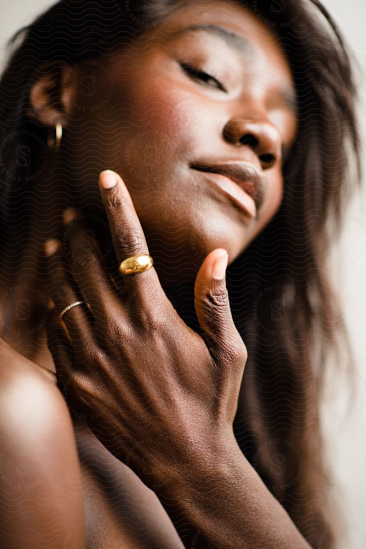 A black woman models a gold band while touching her face.