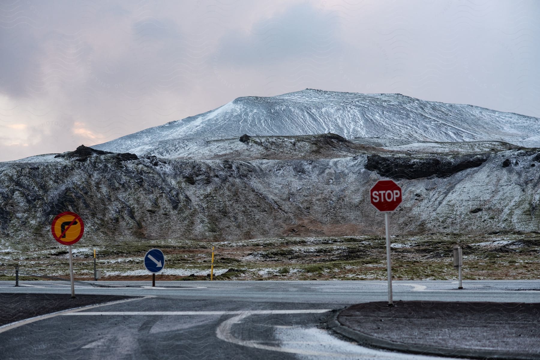 A road near mountain tops covered in snow on a cloudy day