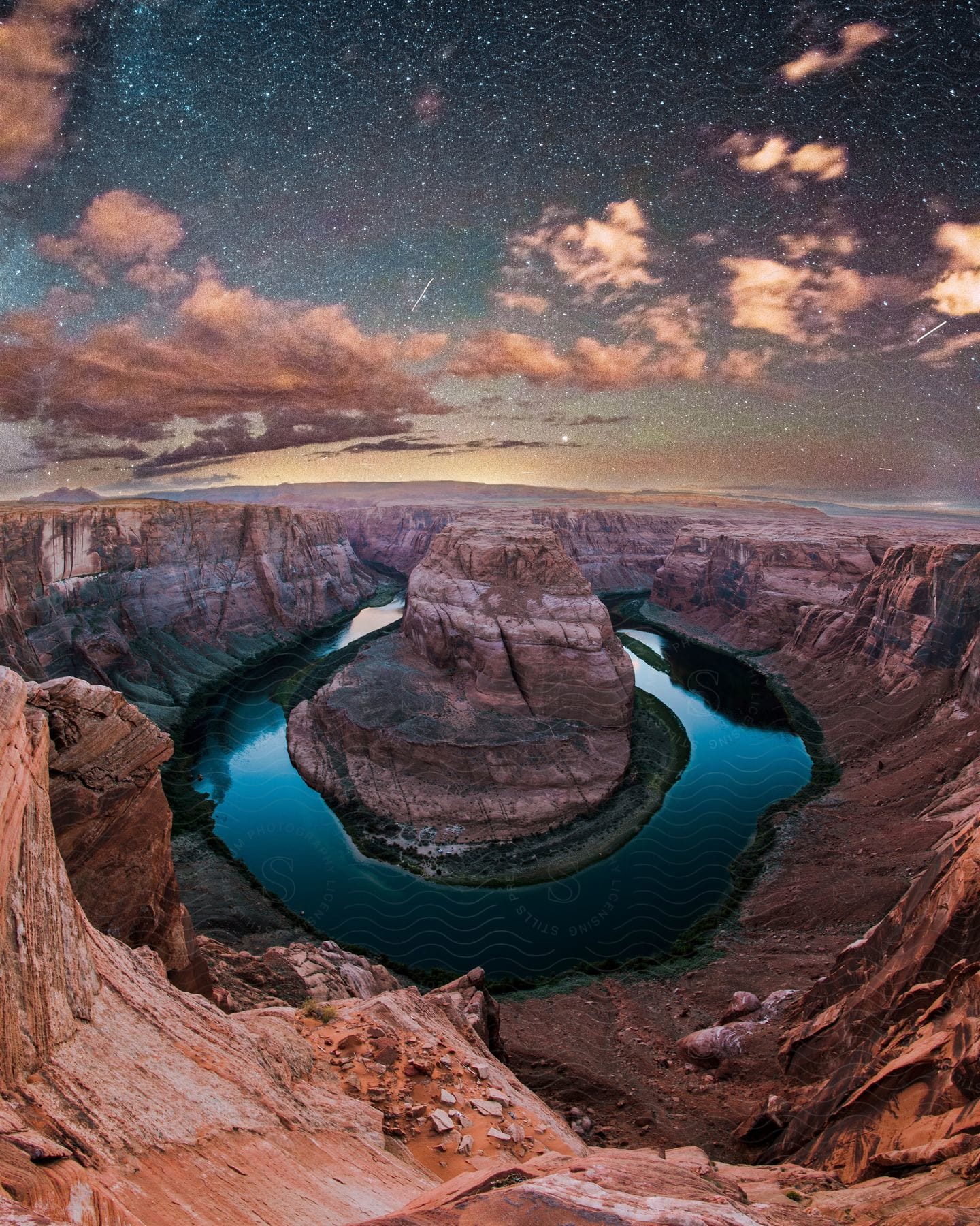 Lake in the mountains with a rock formation island in the center as stars glow among clouds in the sky