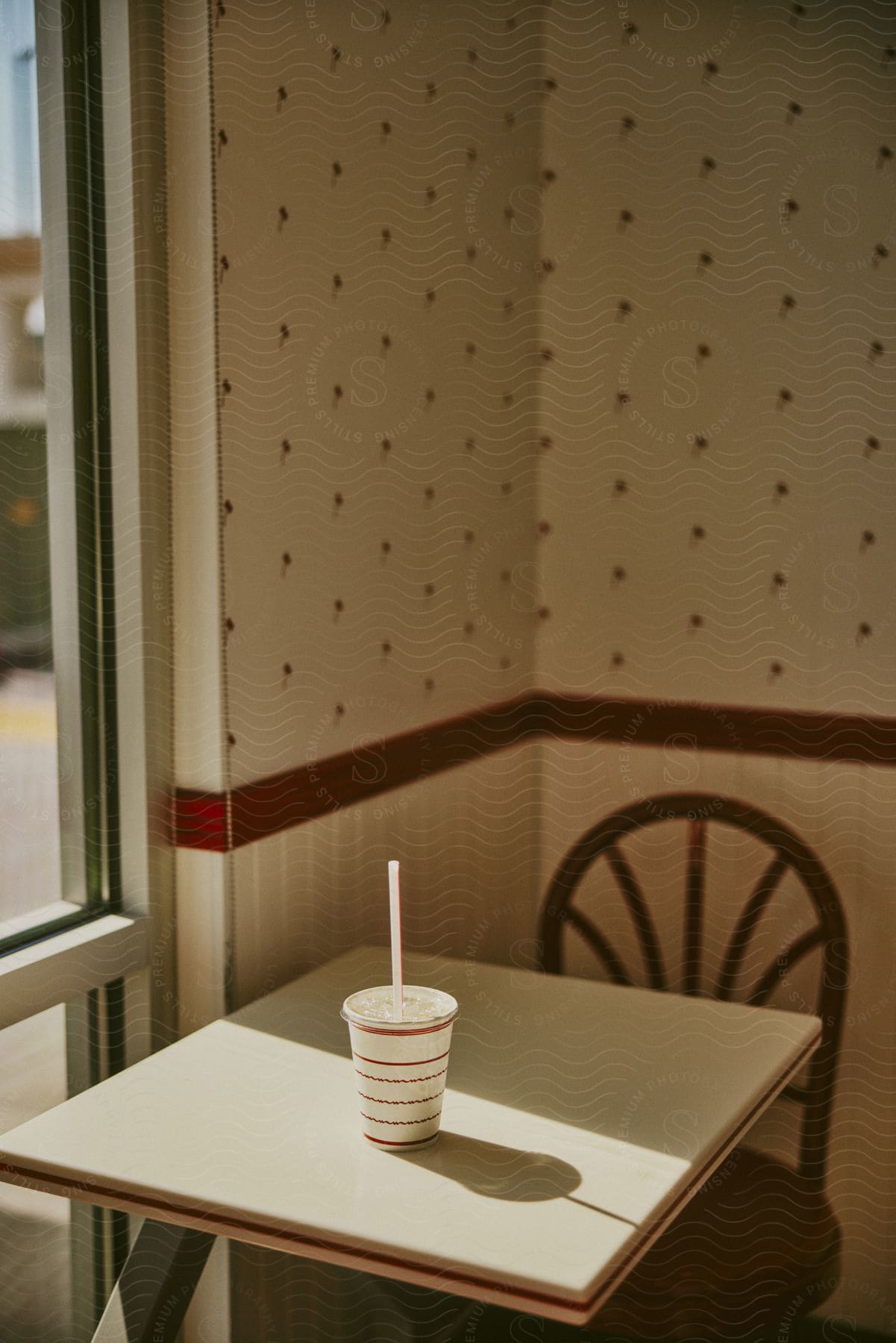 Disposable soda cup sits on small table near window in restaurant.