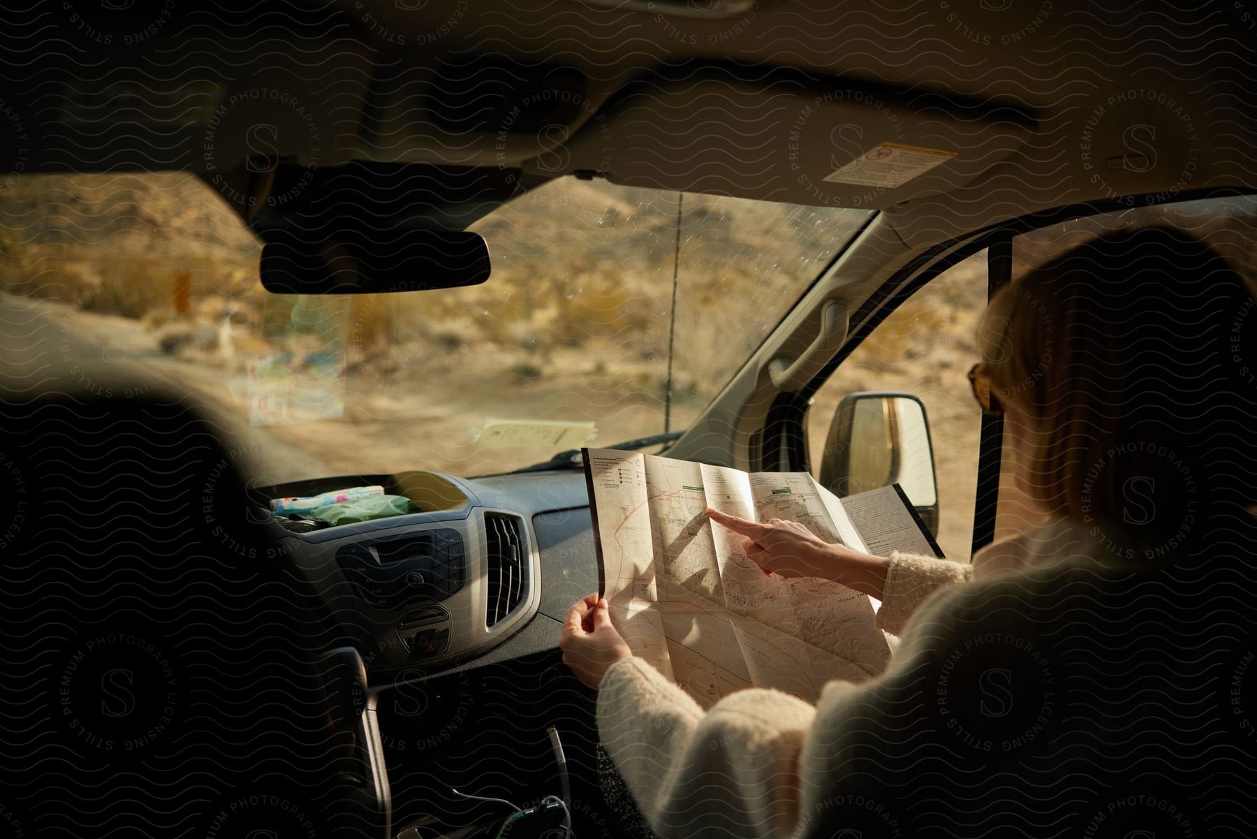 Woman in passenger seat reading a map inside car with desert landscape visible outside.